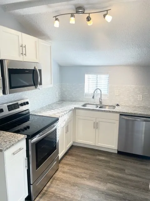 Modern kitchen featuring white cabinetry, light-toned countertops, stainless steel appliances, and wood-finish flooring