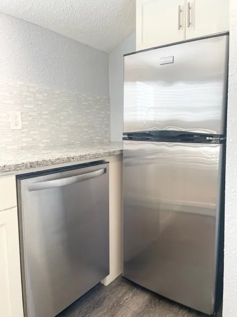 Kitchen featuring stainless steel appliances, white cabinetry with silver hardware, speckled countertops, and a mosaic tile backsplash