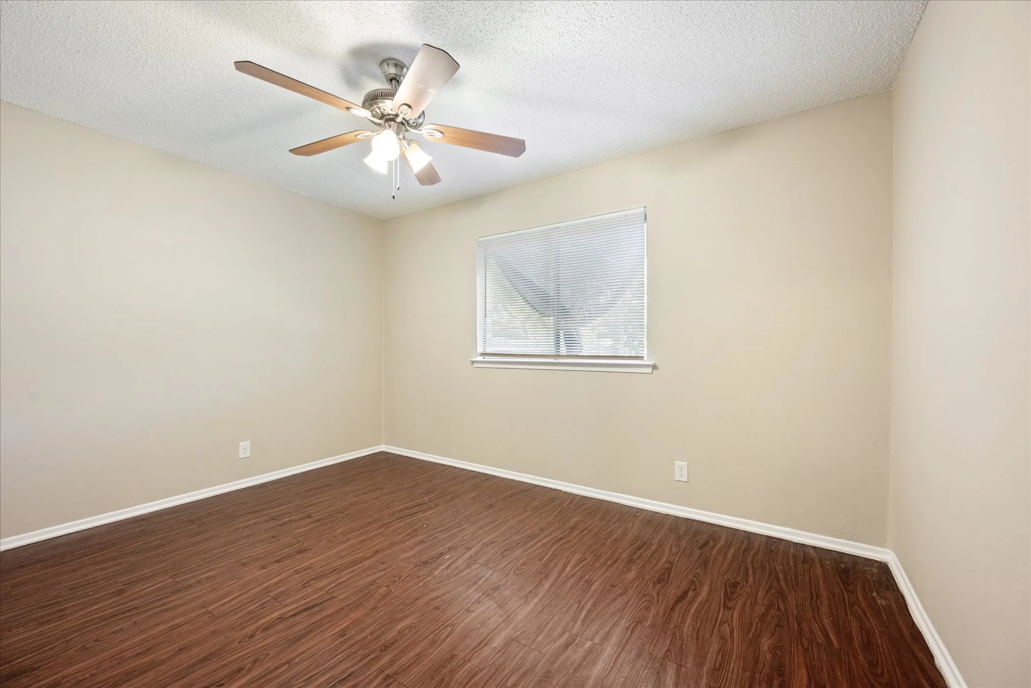 Room with wood-finish flooring, neutral-toned walls, and a ceiling fan with integrated lighting