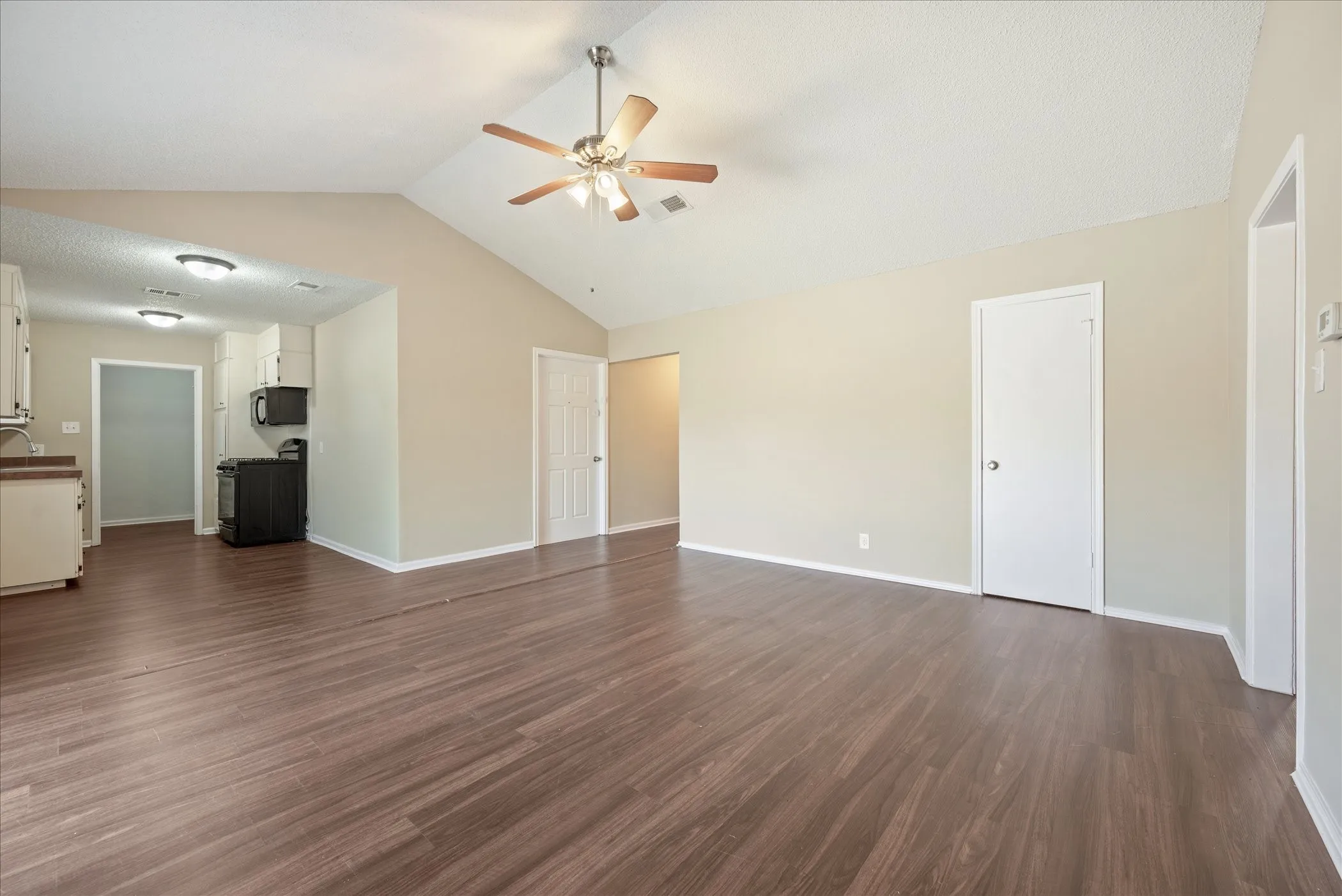 Spacious living area featuring vaulted ceilings, wood-finish flooring, a ceiling fan with integrated lighting, and an open layout to the kitchen