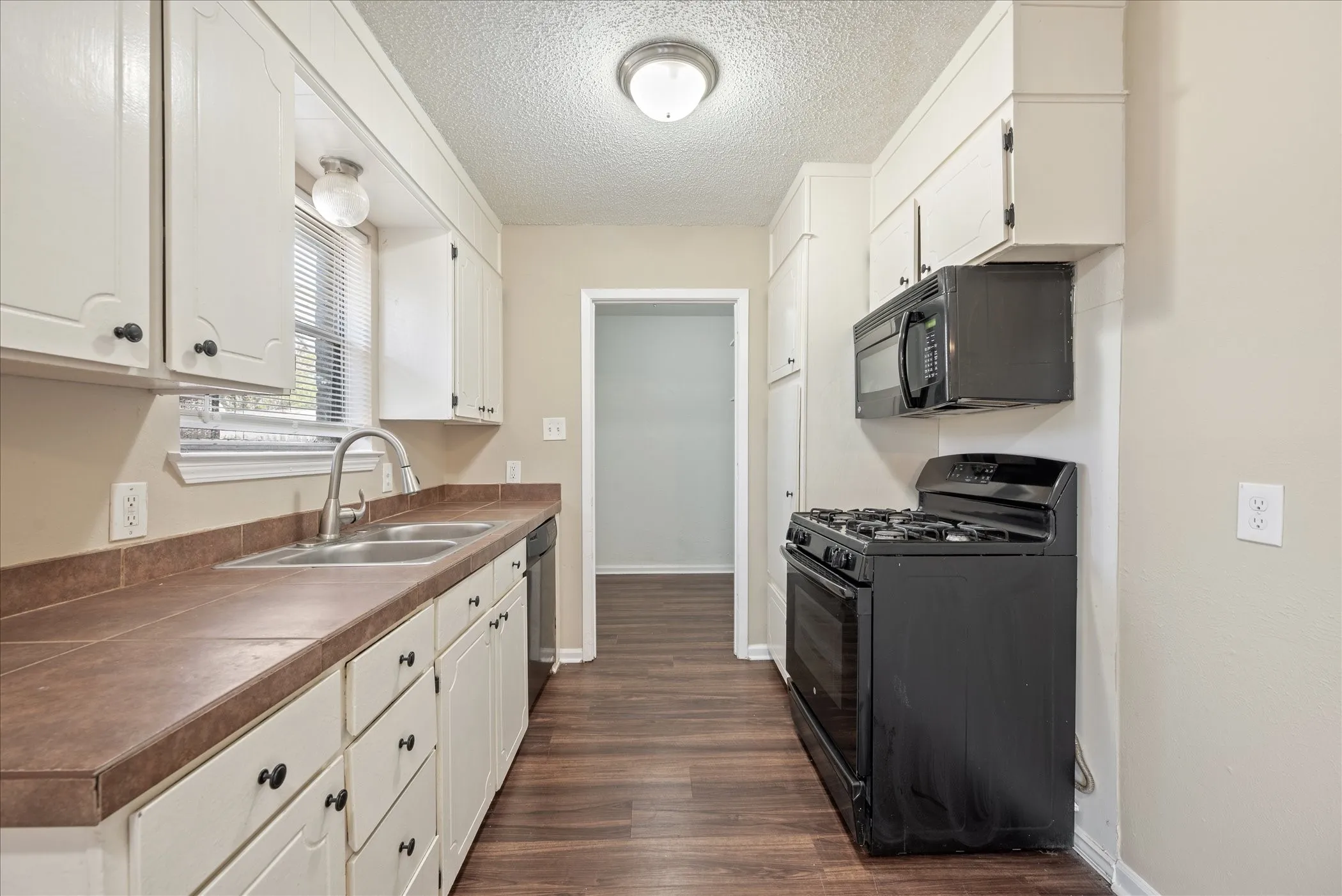 Kitchen featuring white cabinetry, wood-finish flooring, a double basin stainless steel sink, dark countertops, and black appliances including a gas range and microwave