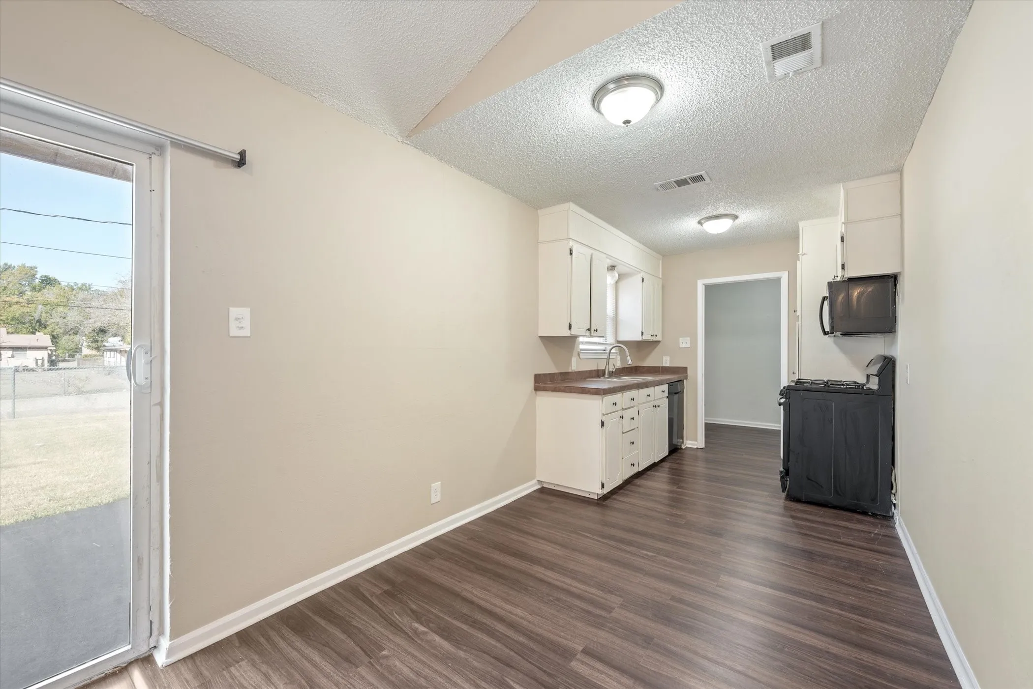 Kitchen area featuring wood-finish flooring, white cabinetry, integrated sink, and an overhead microwave