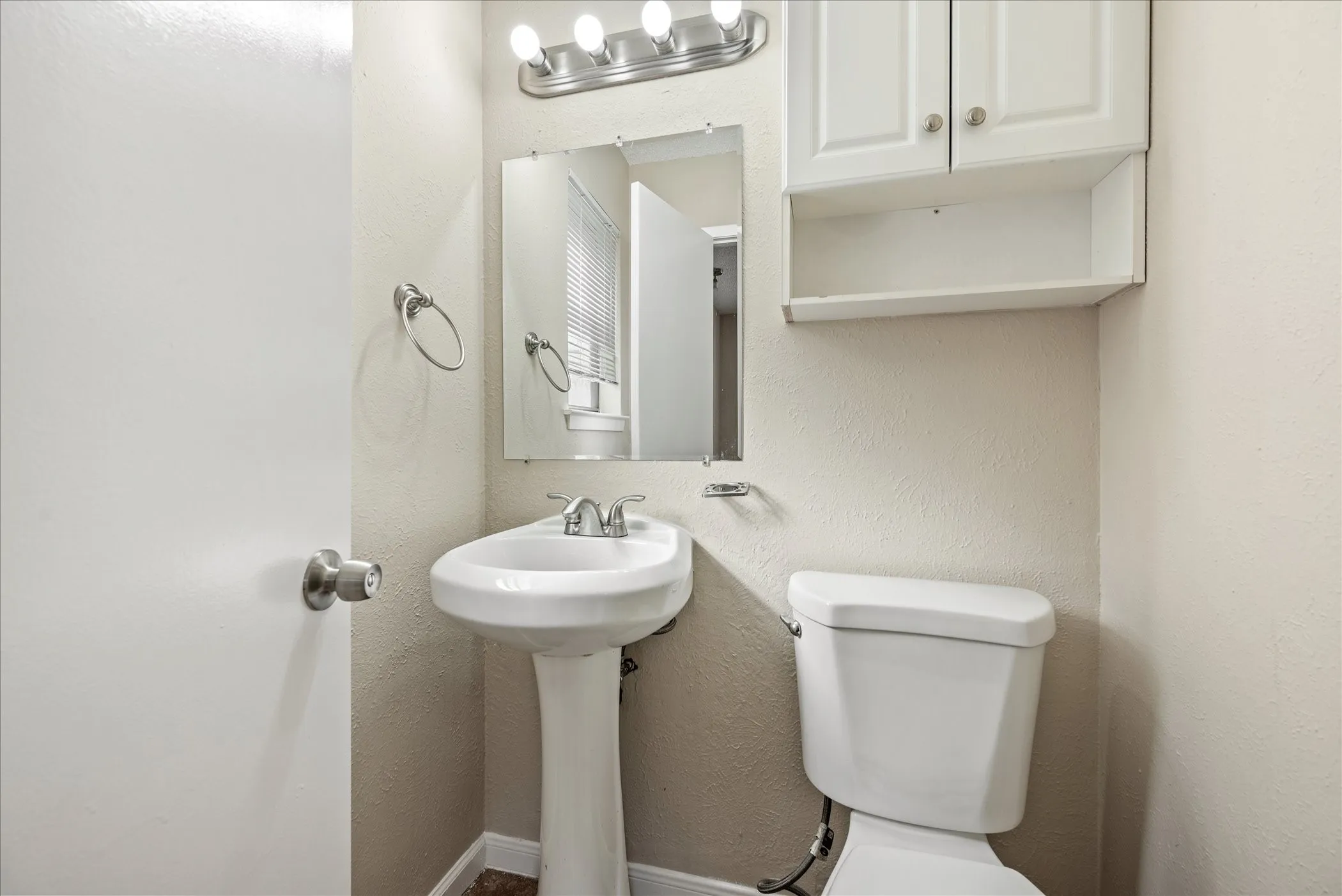 Pedestal sink with chrome fixtures, a wall-mounted mirror, and overhead vanity lighting
