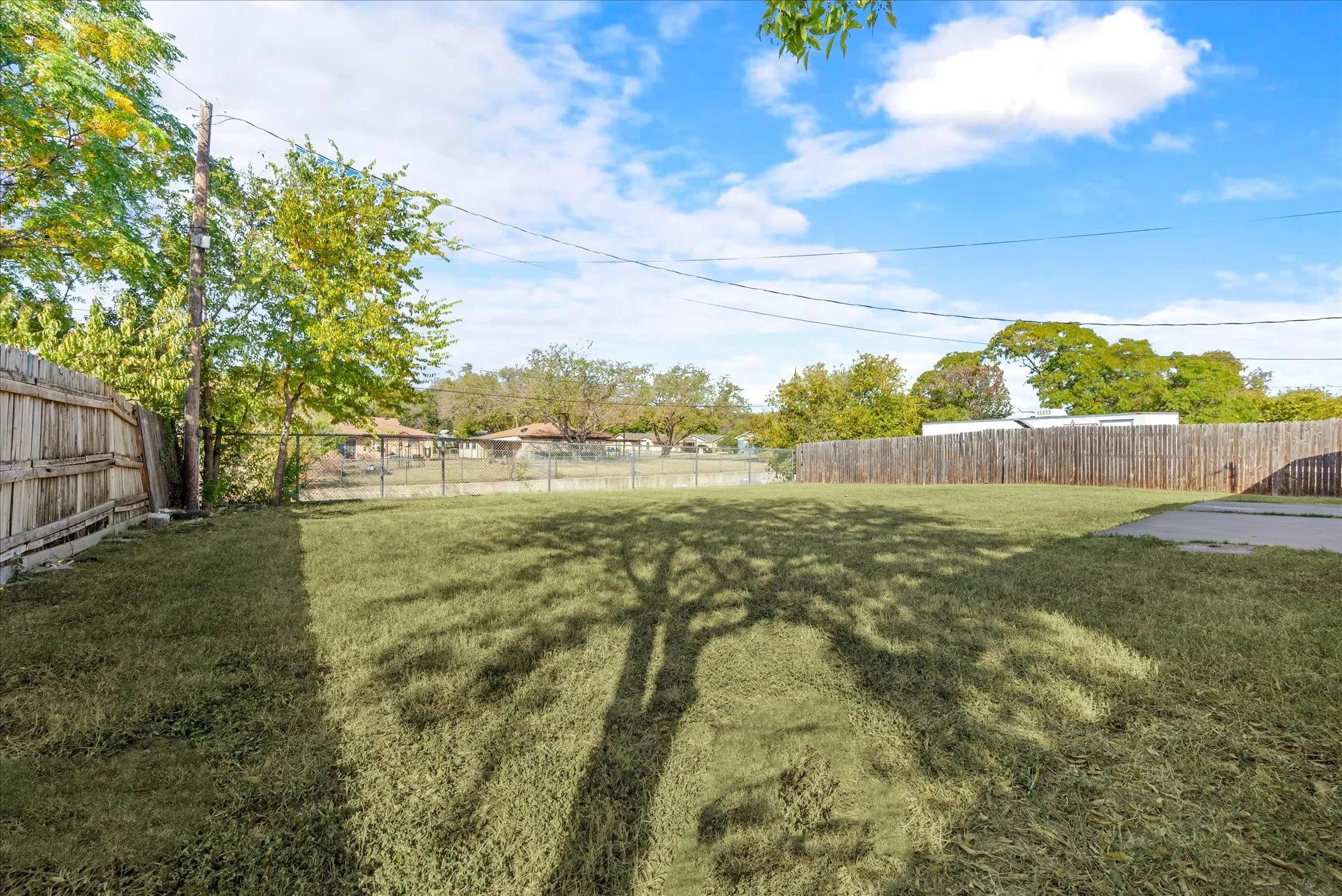 Expansive grass lawn featuring a partial wood privacy fence, a partial chain-link fence, and mature trees