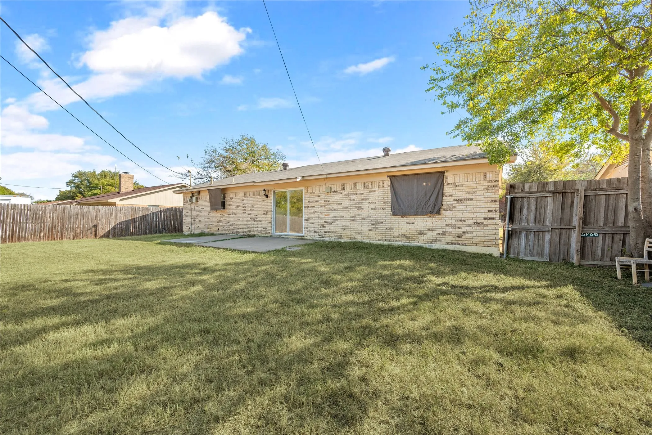 Expansive grassy yard with mature trees and a wood privacy fence