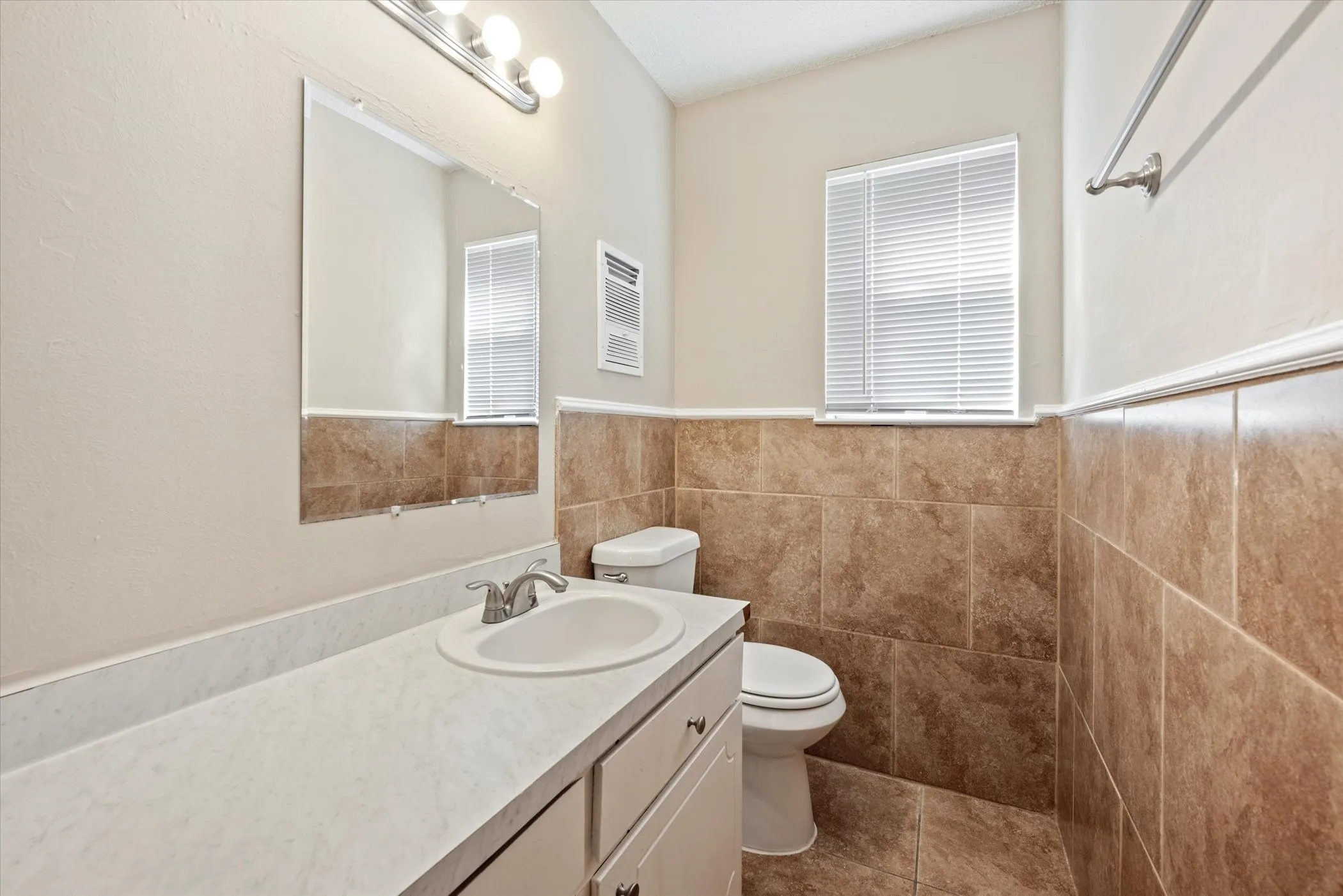 Bathroom featuring a white vanity with an integrated sink, a rectangular mirror, a three-light vanity bar, a window with blinds, and floor-to-ceiling tile