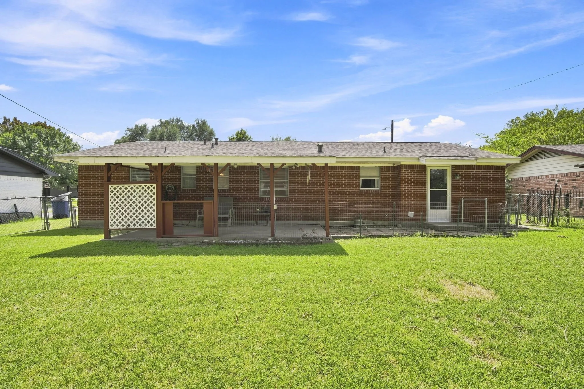 Expansive rear lawn featuring a covered concrete patio, brick exterior, and white lattice privacy screen
