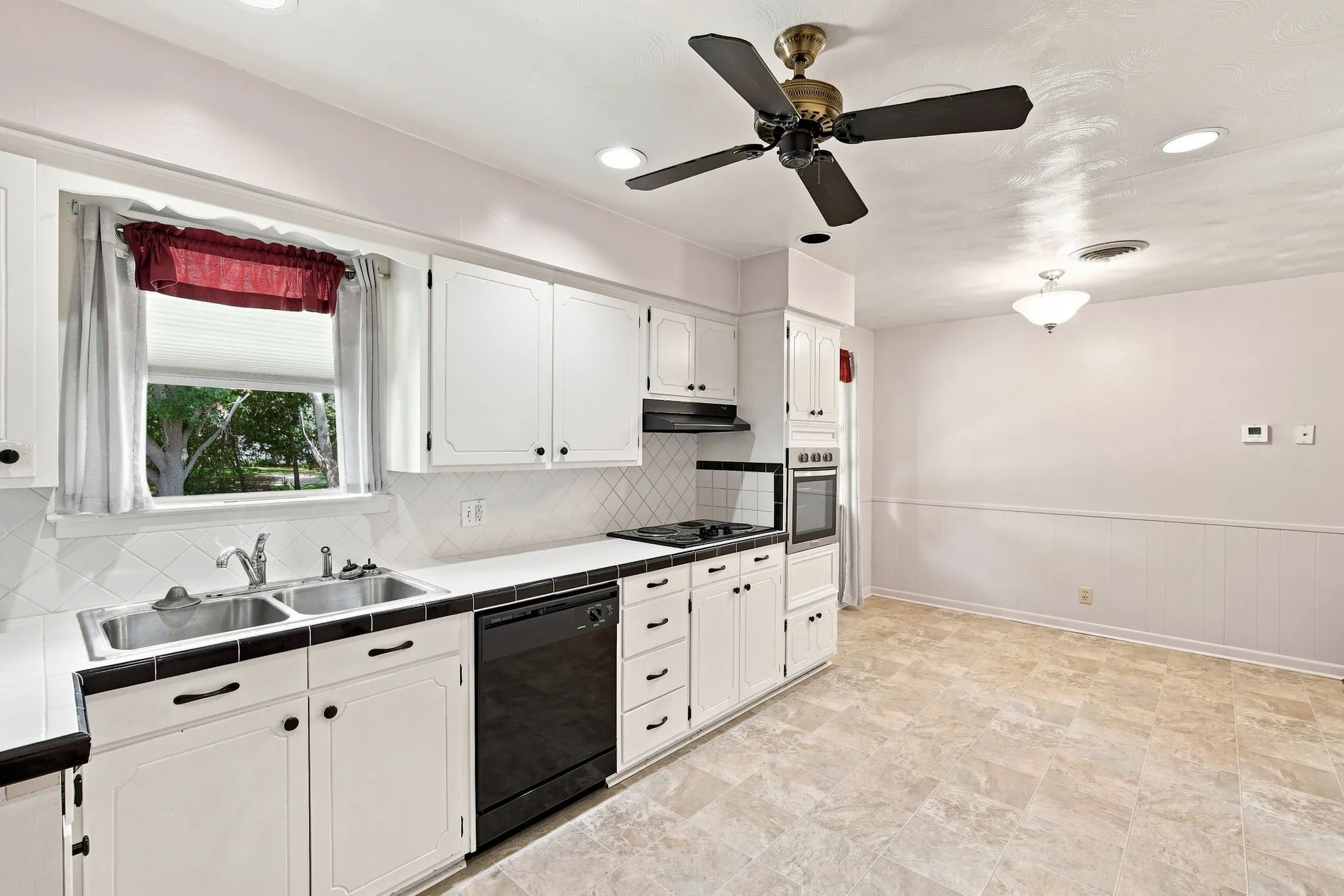Kitchen space featuring white cabinetry with black hardware, a dual basin sink, black built-in appliances, and a tiled backsplash