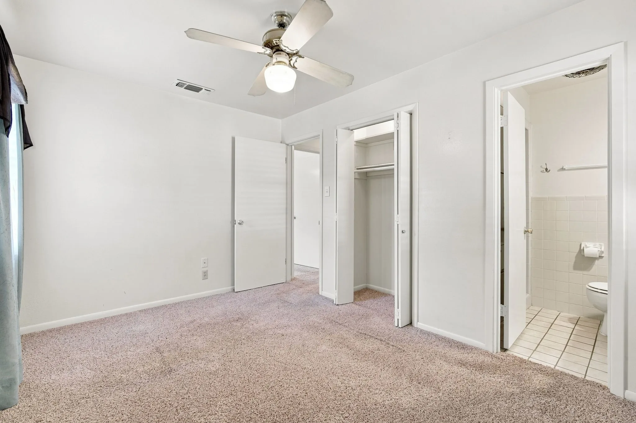 Carpeted room with white walls, a ceiling fan, and a window with light-colored curtains