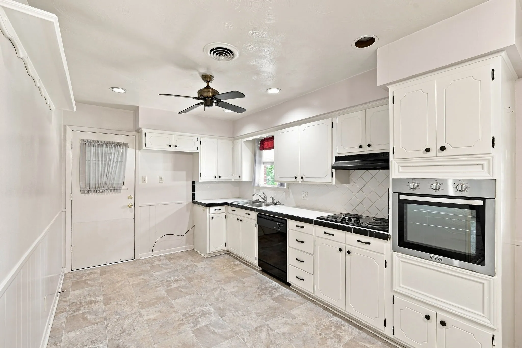 Kitchen featuring white cabinetry, black countertops, a built-in oven, tile backsplash, and a ceiling fan