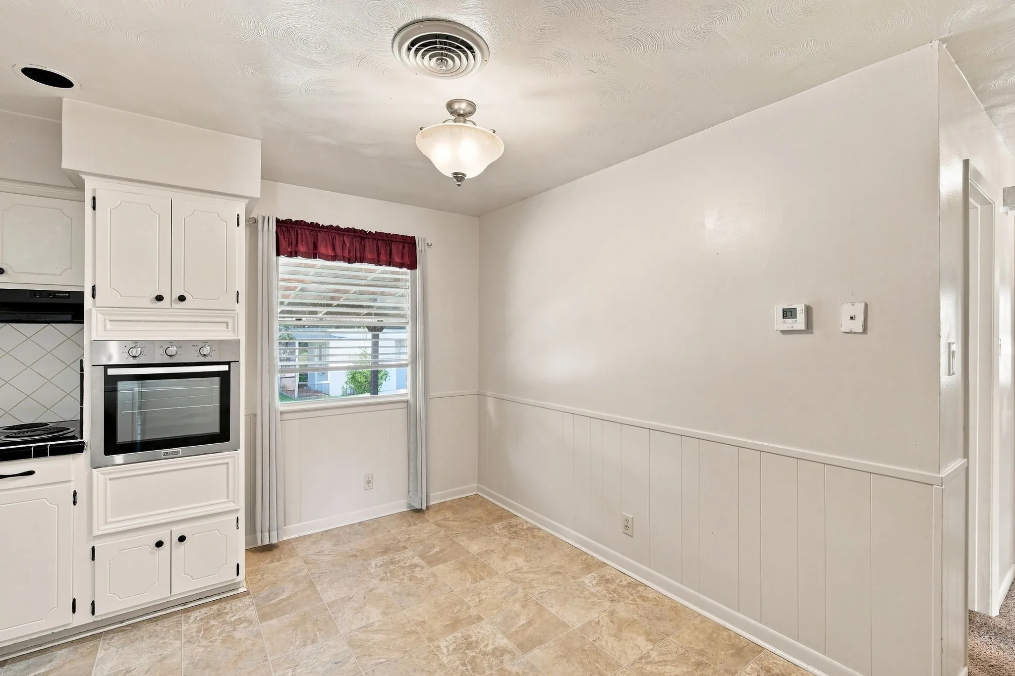 Kitchen and dining area featuring a built-in oven, white cabinetry, a window with blinds, and tile flooring