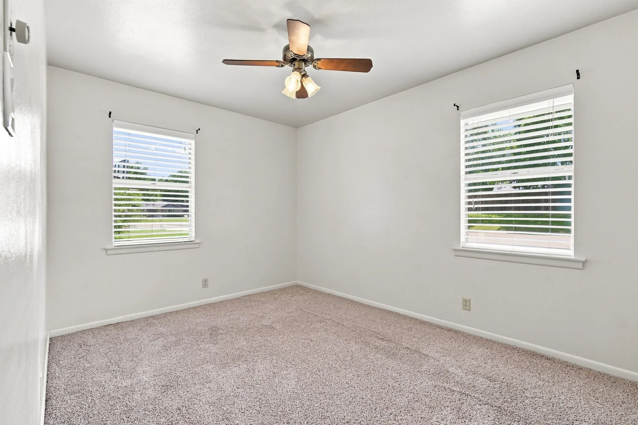 Carpeted room featuring two windows with horizontal blinds, a ceiling fan with integrated lighting, and neutral wall tones