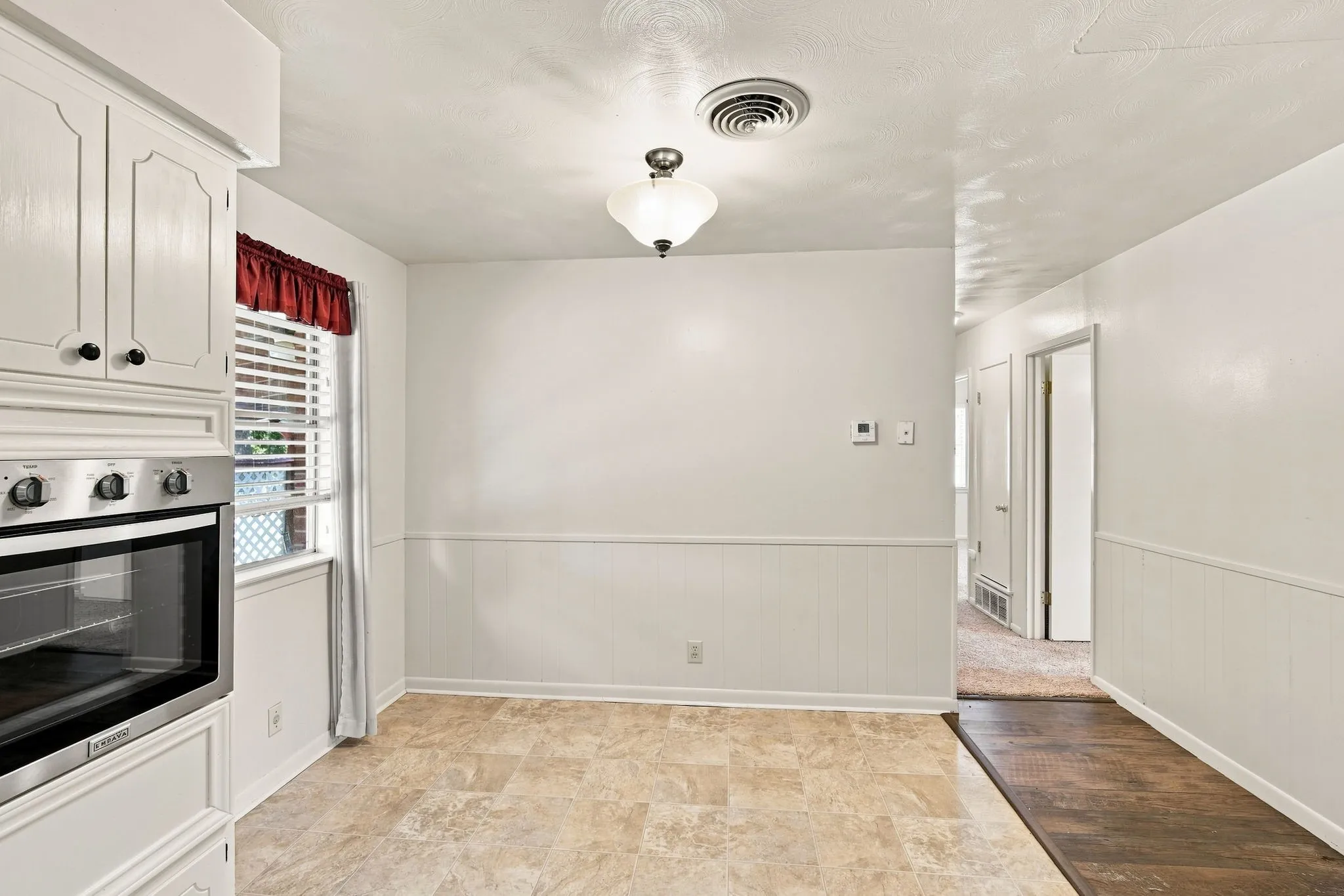 Eat-in kitchen area featuring durable tile-look flooring, wainscoting, and a window with blinds