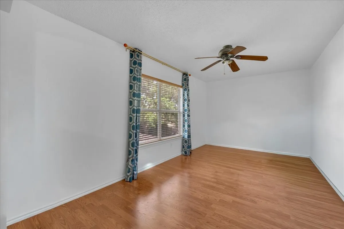 Wood-finish flooring, ceiling fan, and large window with blinds