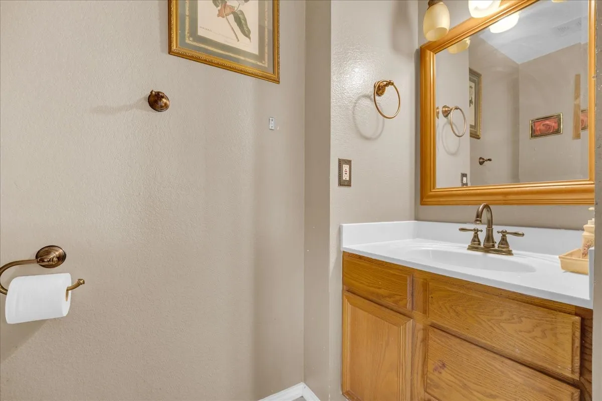 Wood-finish vanity with a white countertop and integrated sink, framed mirror, and wall-mounted light fixture
