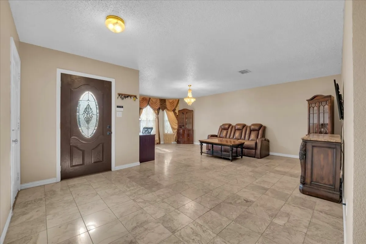 Spacious room featuring tile flooring, a decorative entry door with an oval glass insert, and a chandelier in the background