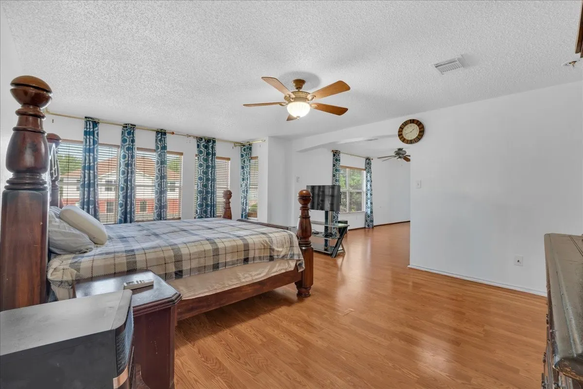 Expansive room with wood-finish flooring, multiple windows, and two ceiling fans