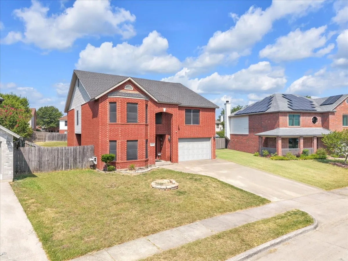 Red brick exterior featuring a front-facing garage, a paved driveway, and a front yard with a built-in fire pit