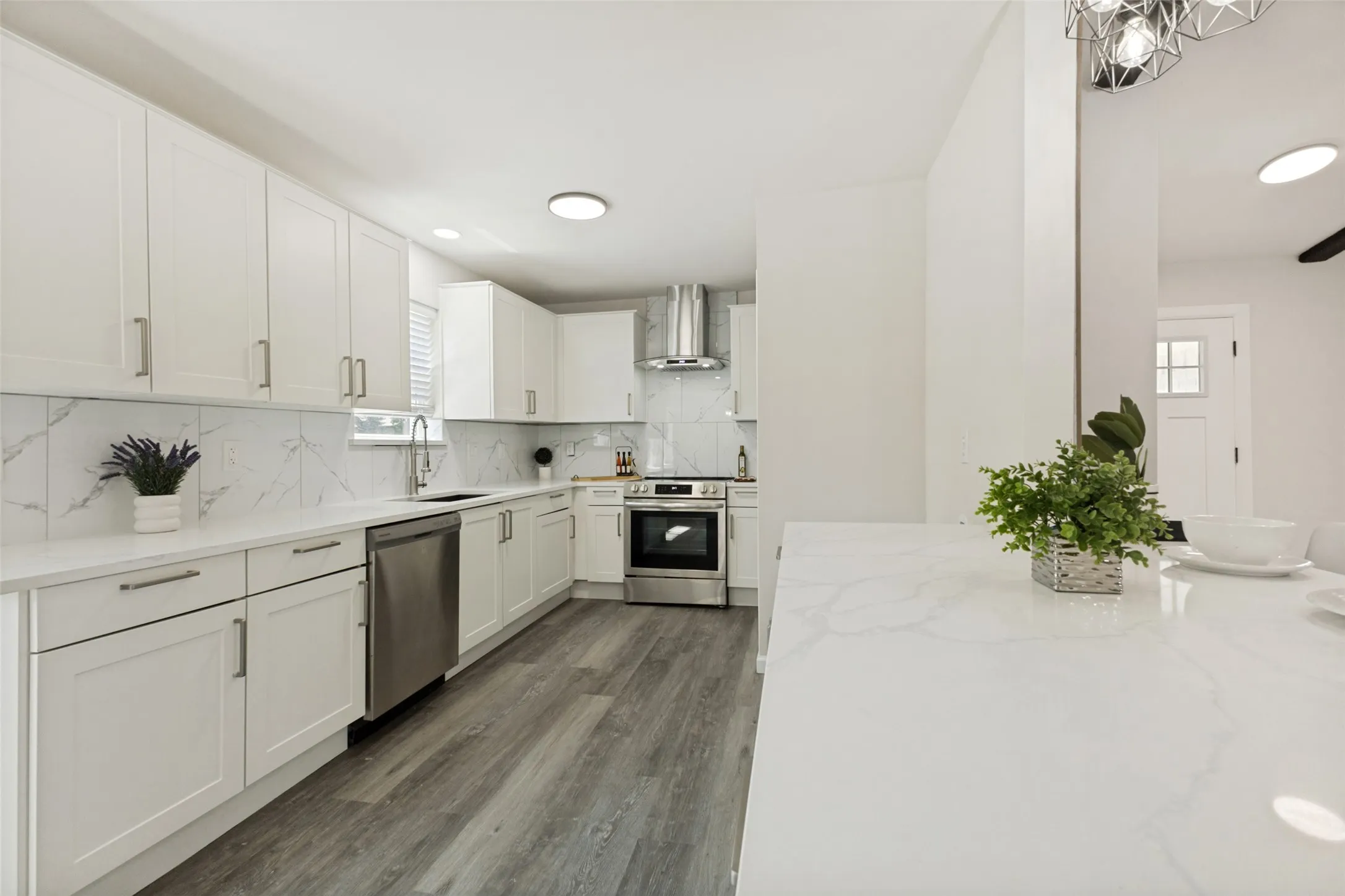 Modern kitchen featuring white shaker cabinetry, stainless steel appliances, and wood-finish flooring