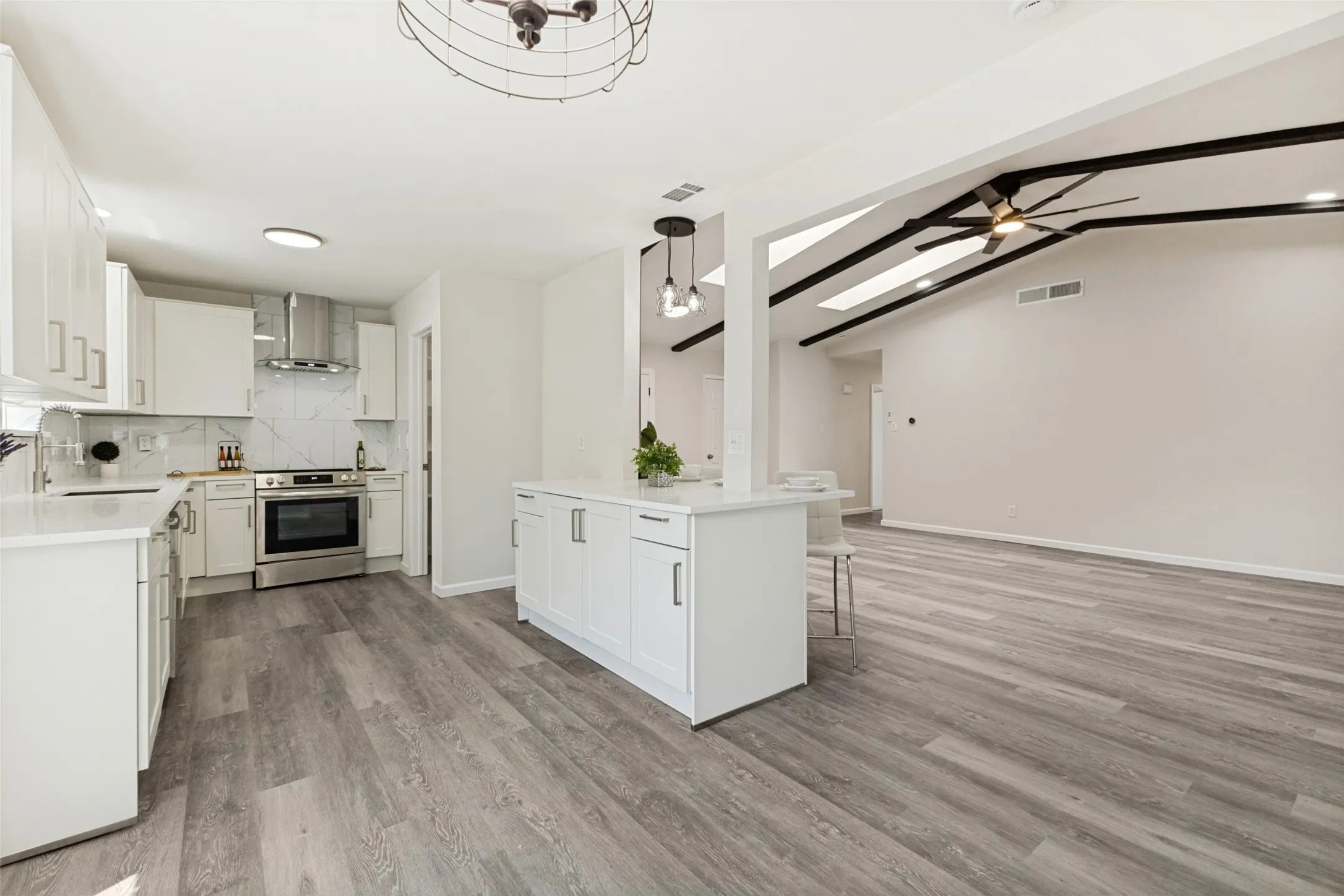 Open concept kitchen and living area featuring white cabinetry, stainless steel appliances, stone countertops, and wood-finish flooring