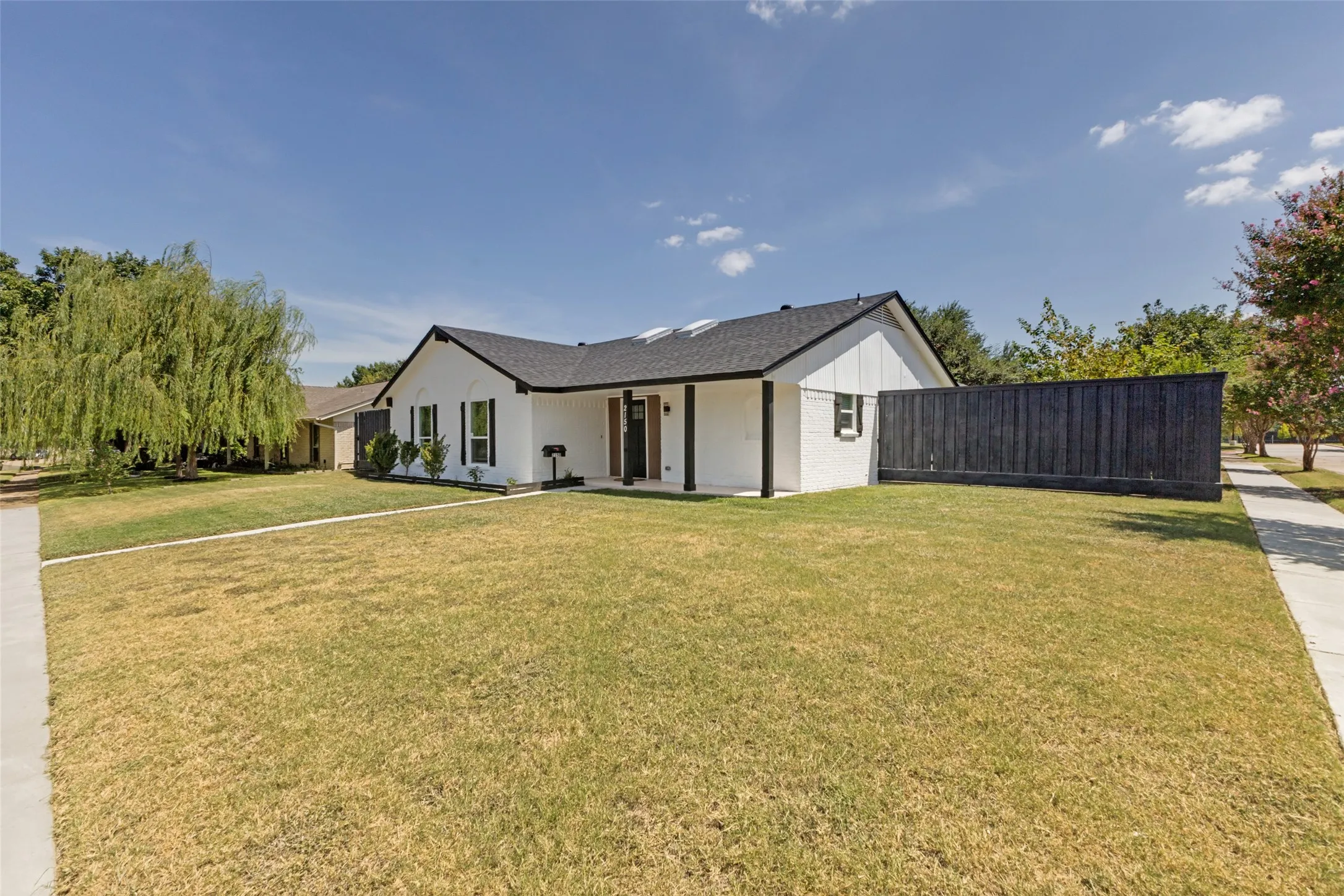 White exterior residence with a dark shingle roof, black trim, and a dark privacy fence