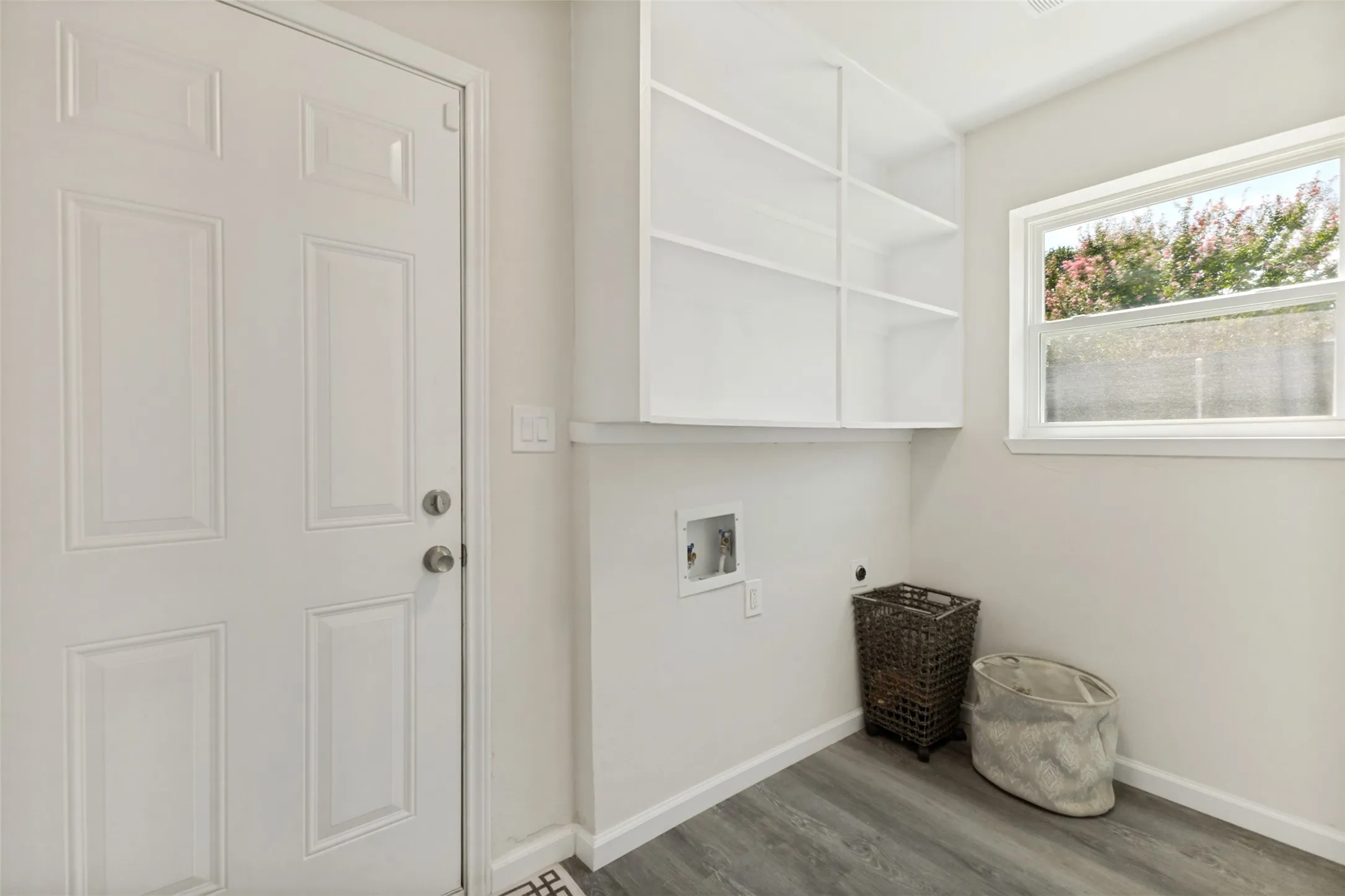 Dedicated laundry space featuring a window, built-in shelving, wood-finish flooring, and a paneled door
