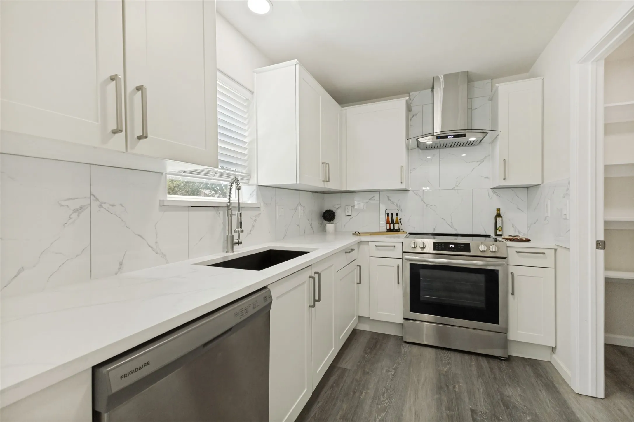 Modern kitchen featuring white shaker cabinetry, white countertops, marble-look backsplash, stainless steel appliances, and wood-finish flooring