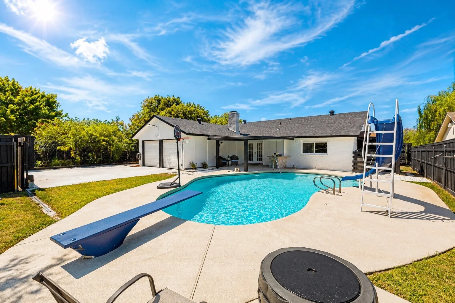 Expansive backyard featuring a freeform swimming pool with a diving board and slide, surrounded by a concrete patio