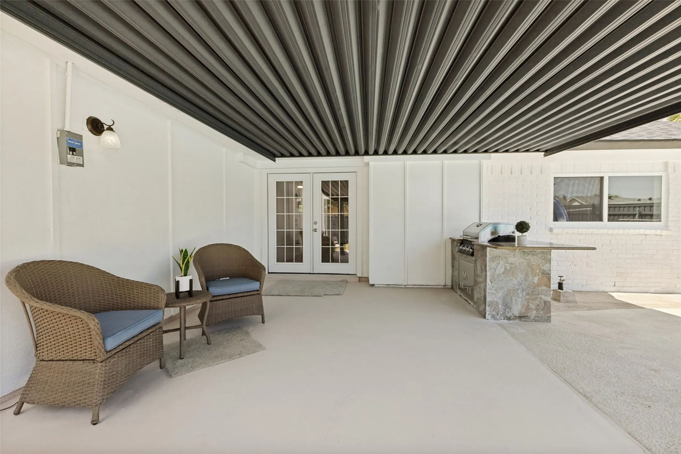 Covered patio area featuring a slatted ceiling, white exterior walls, and a stone-clad outdoor kitchen with a built-in grill