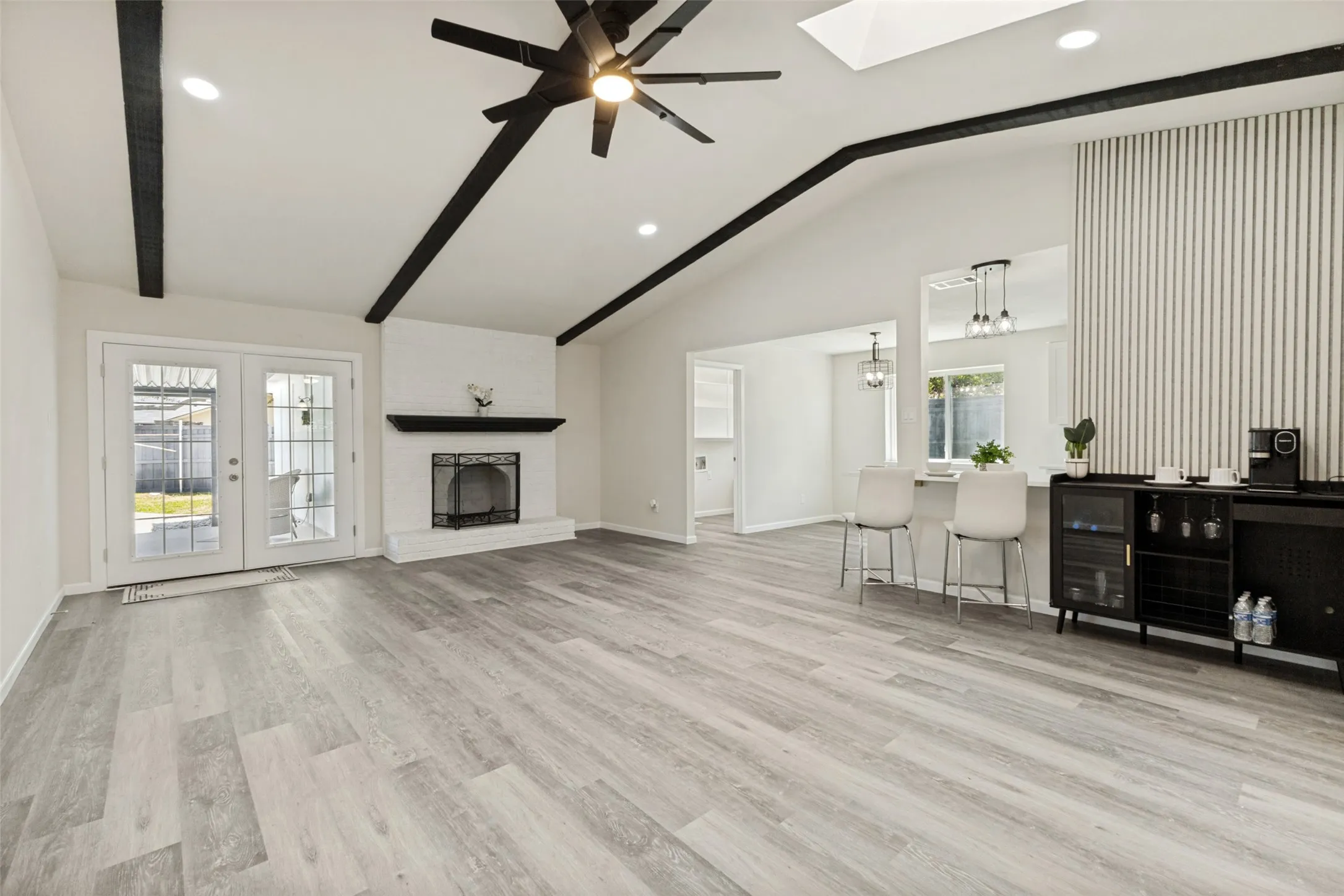 Spacious living area featuring vaulted ceilings with exposed beams, wood-finish flooring, and a white brick fireplace