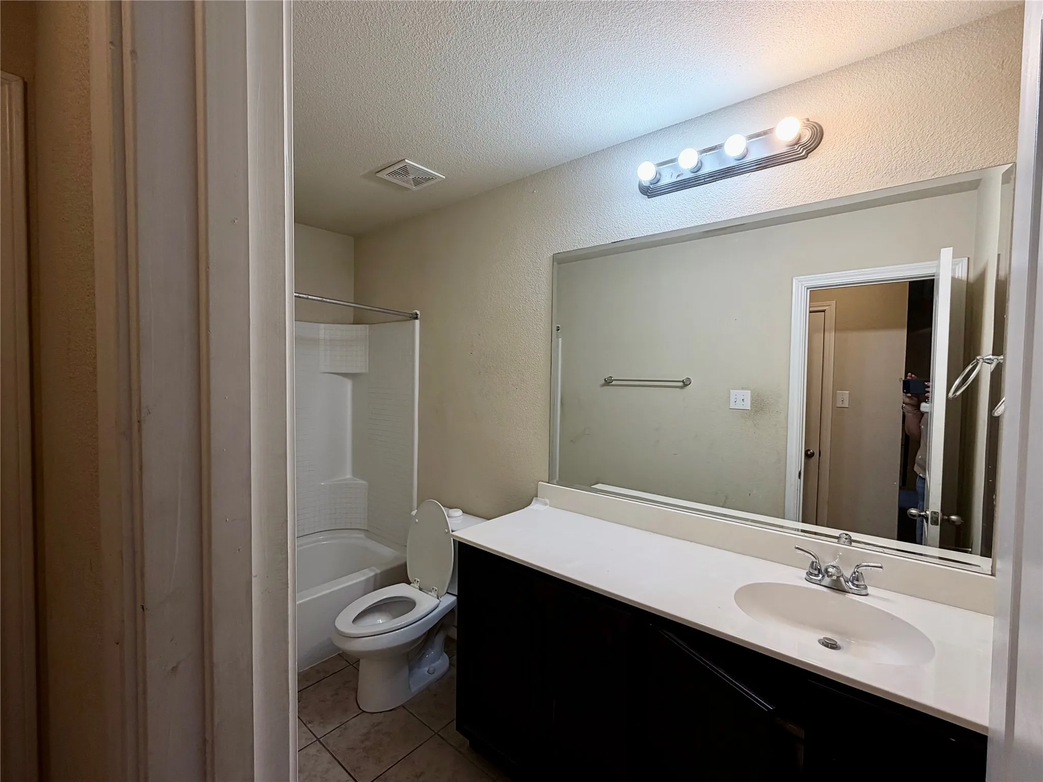 Bathroom featuring a white bathtub and shower combination, a single vanity with an integrated sink, a large wall-mounted mirror, and tile flooring
