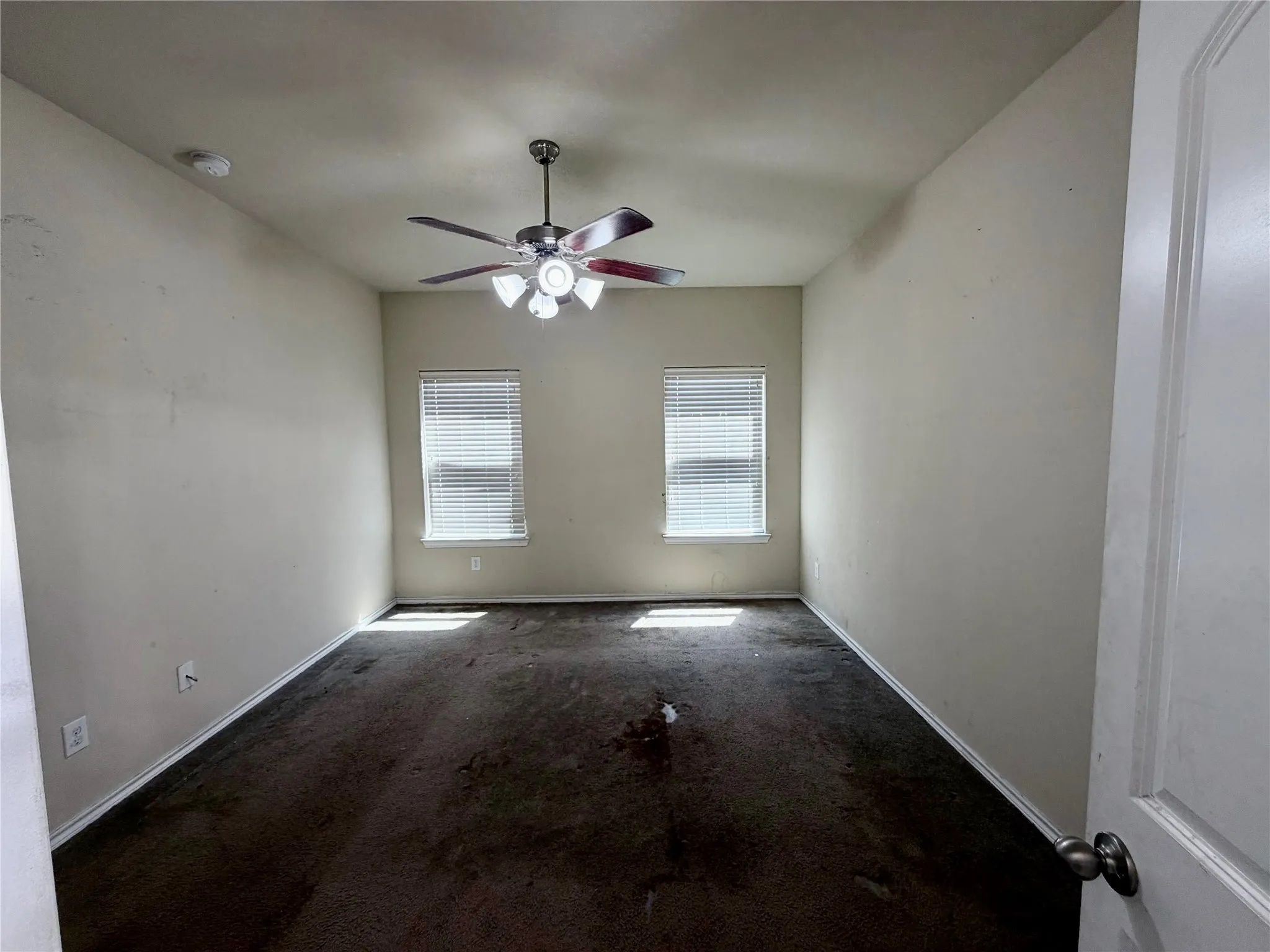 Spacious room featuring two windows with white blinds, a ceiling fan with integrated lighting, and neutral-toned walls