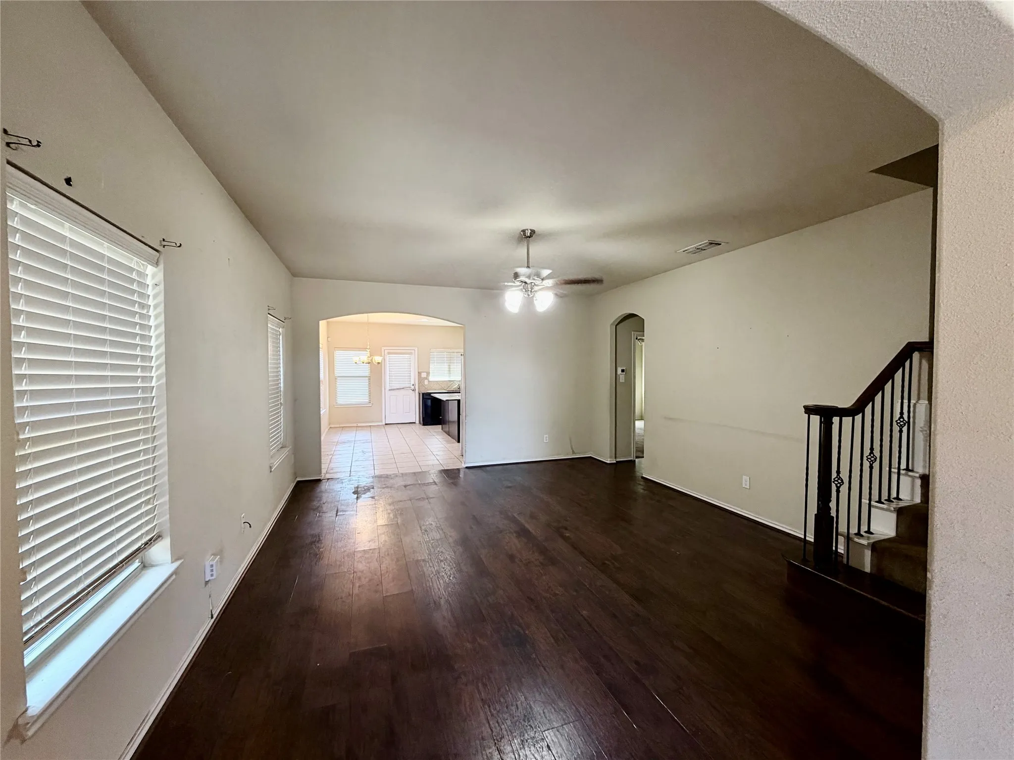 Spacious interior room featuring dark wood-finish flooring, light neutral wall tones, and arched doorways