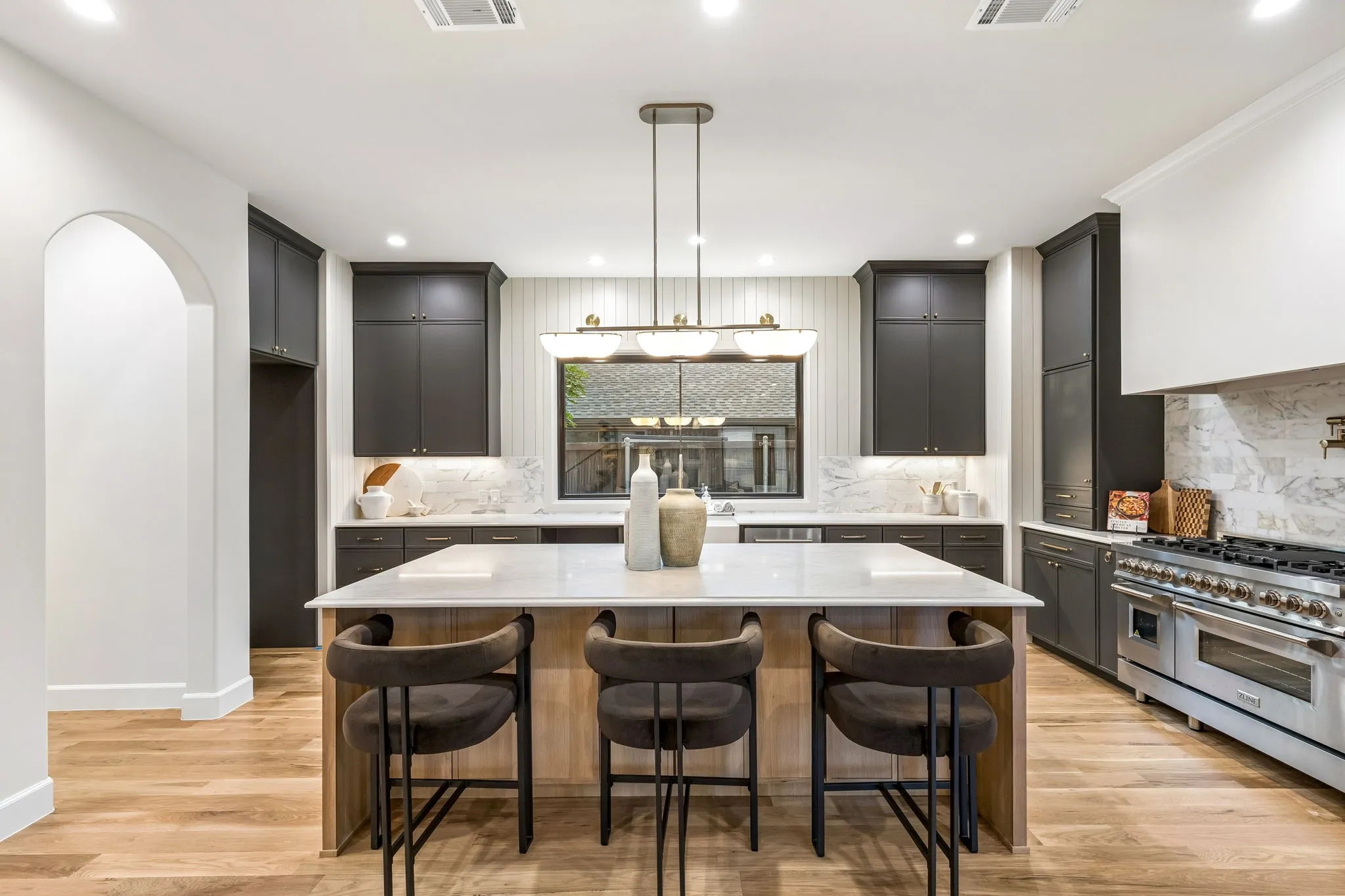 Chef's kitchen with large center island, a picturesque window, designer lighting and custom cabinetry