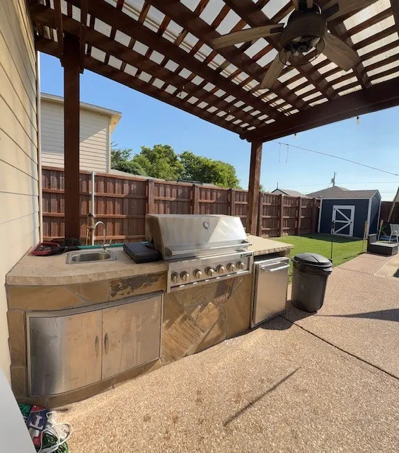 Outdoor kitchen featuring a built-in grill, sink, stainless steel cabinetry, and stone accents