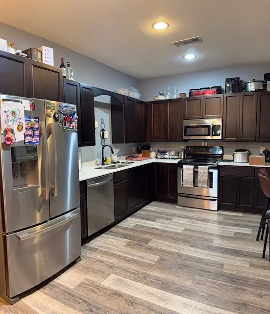 Kitchen featuring dark wood cabinetry, white countertops, stainless steel appliances, and wood-finish flooring
