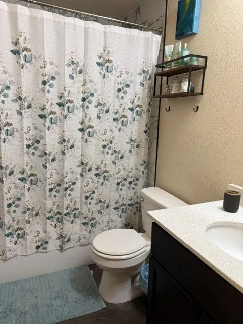 Bathroom featuring dark wood-finish flooring, a white vanity with a light-toned countertop and integrated sink, and a commode