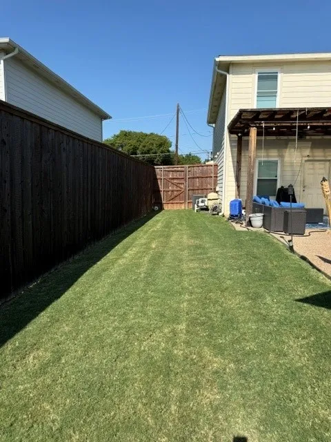 Fenced backyard featuring a manicured lawn, a wooden privacy fence, and a covered patio area with a pergola