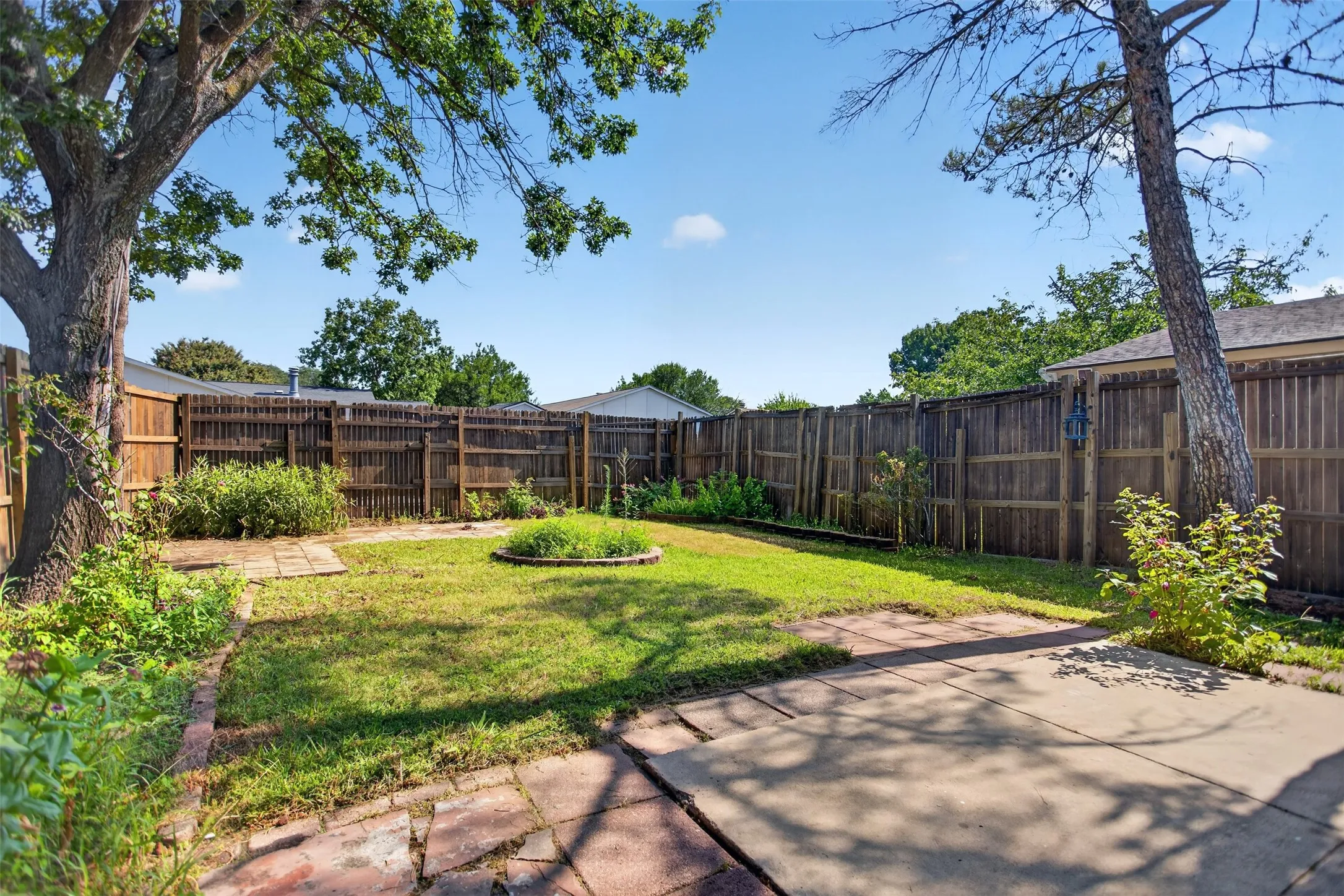 Private fenced backyard featuring a concrete patio and a grass lawn with stone pathways