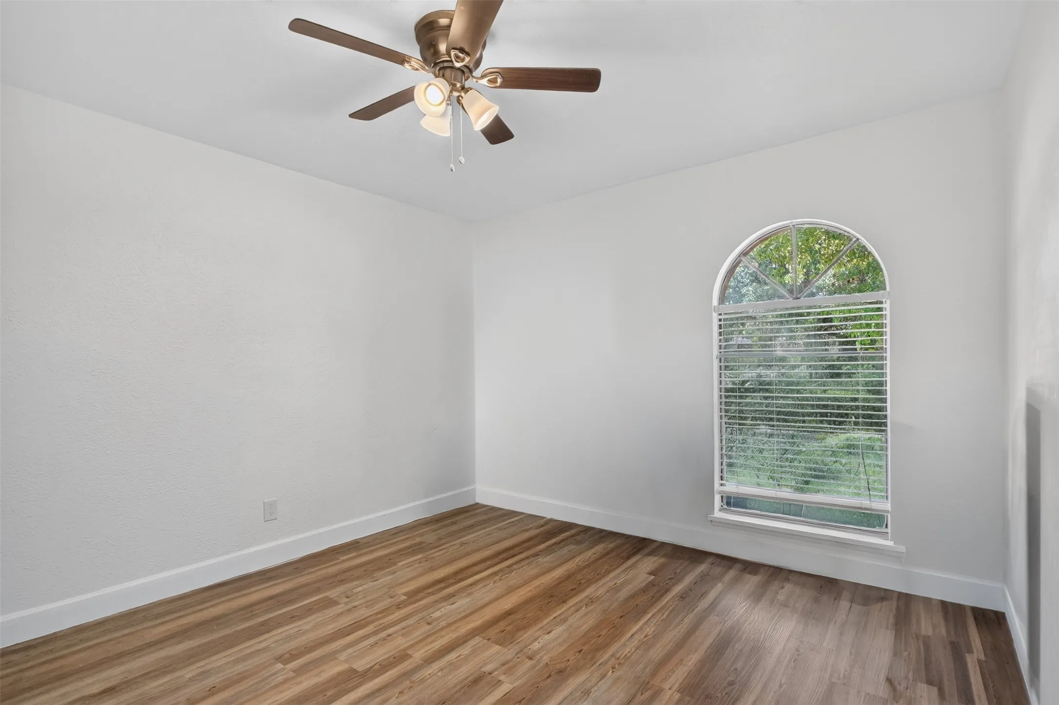 End BedRoom featuring wood-finish flooring, white walls, and a prominent arched window with blinds