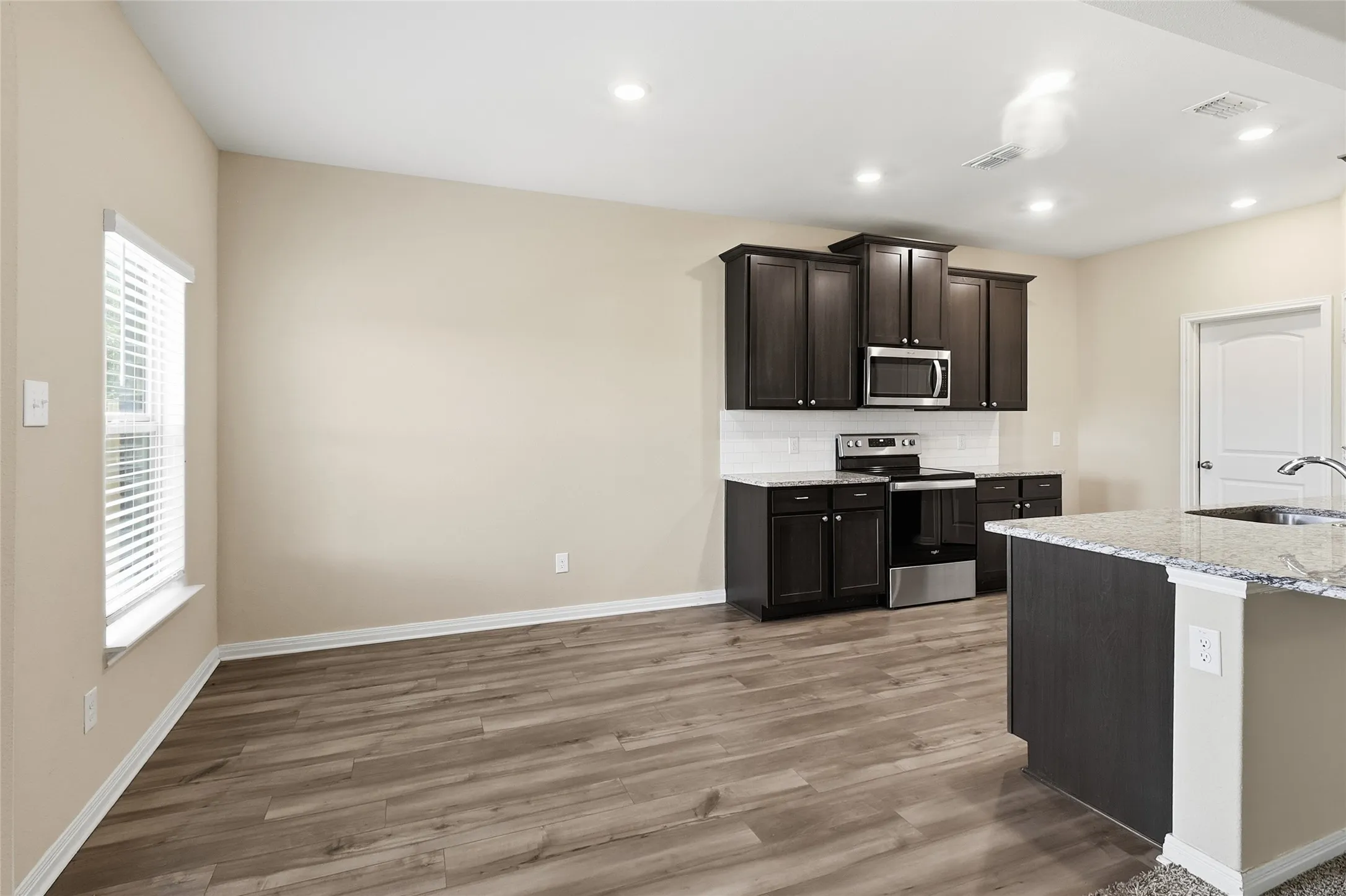 Open-concept living space with wood-finish flooring, recessed lighting, and a window with blinds