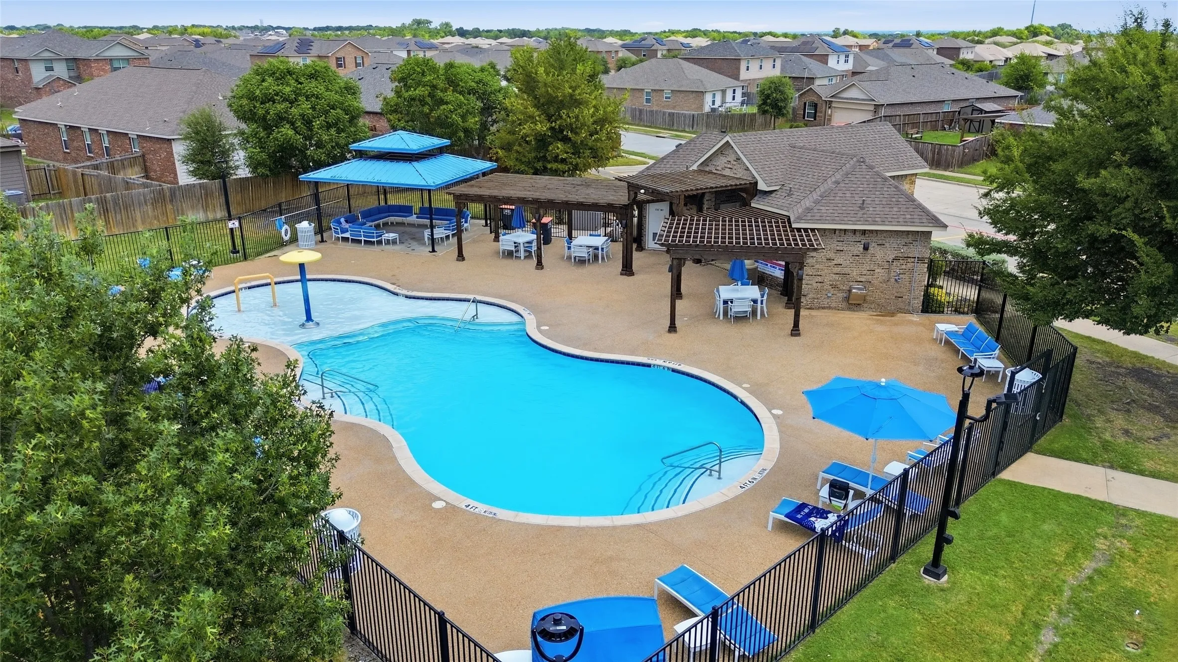 Community Resort-style pool area featuring a freeform swimming pool, separate shallow water play area with a water feature, and a surrounding aggregate deck