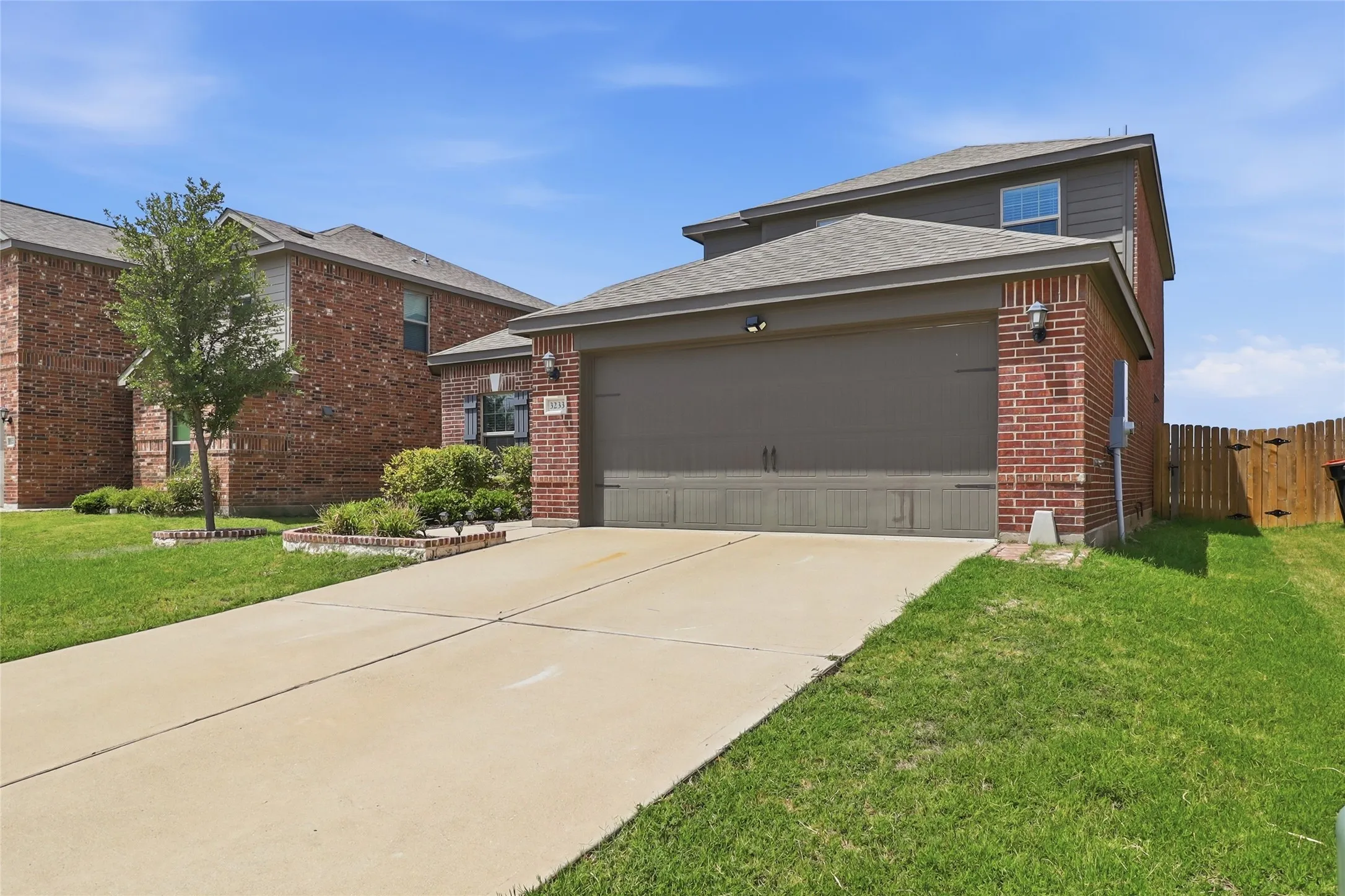 Brick facade two-story residence featuring an attached two-car garage, concrete driveway, and front lawn landscaping
