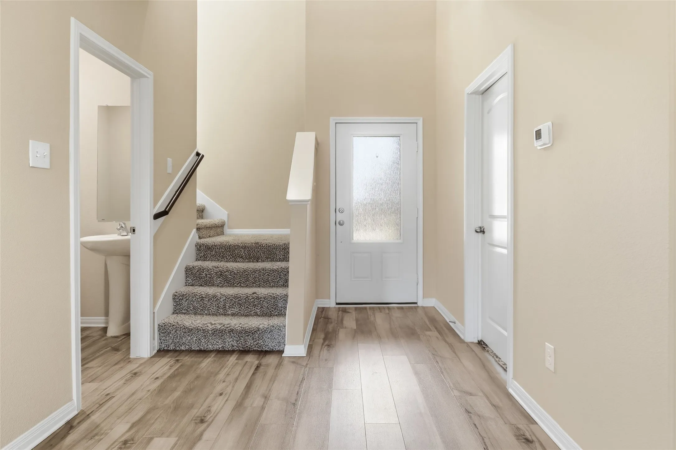 Entryway featuring wood-finish flooring, a carpeted staircase with white risers and a black handrail, and a white panel door with frosted glass