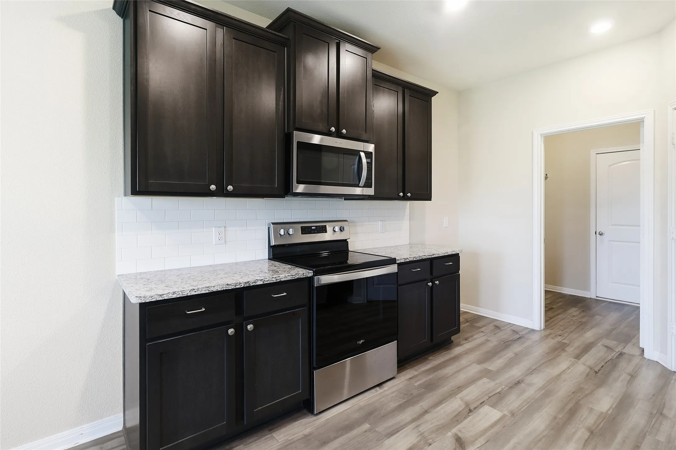 Kitchen featuring dark wood-finish cabinetry, light-toned countertops, subway tile backsplash, stainless steel microwave, and stainless steel electric range