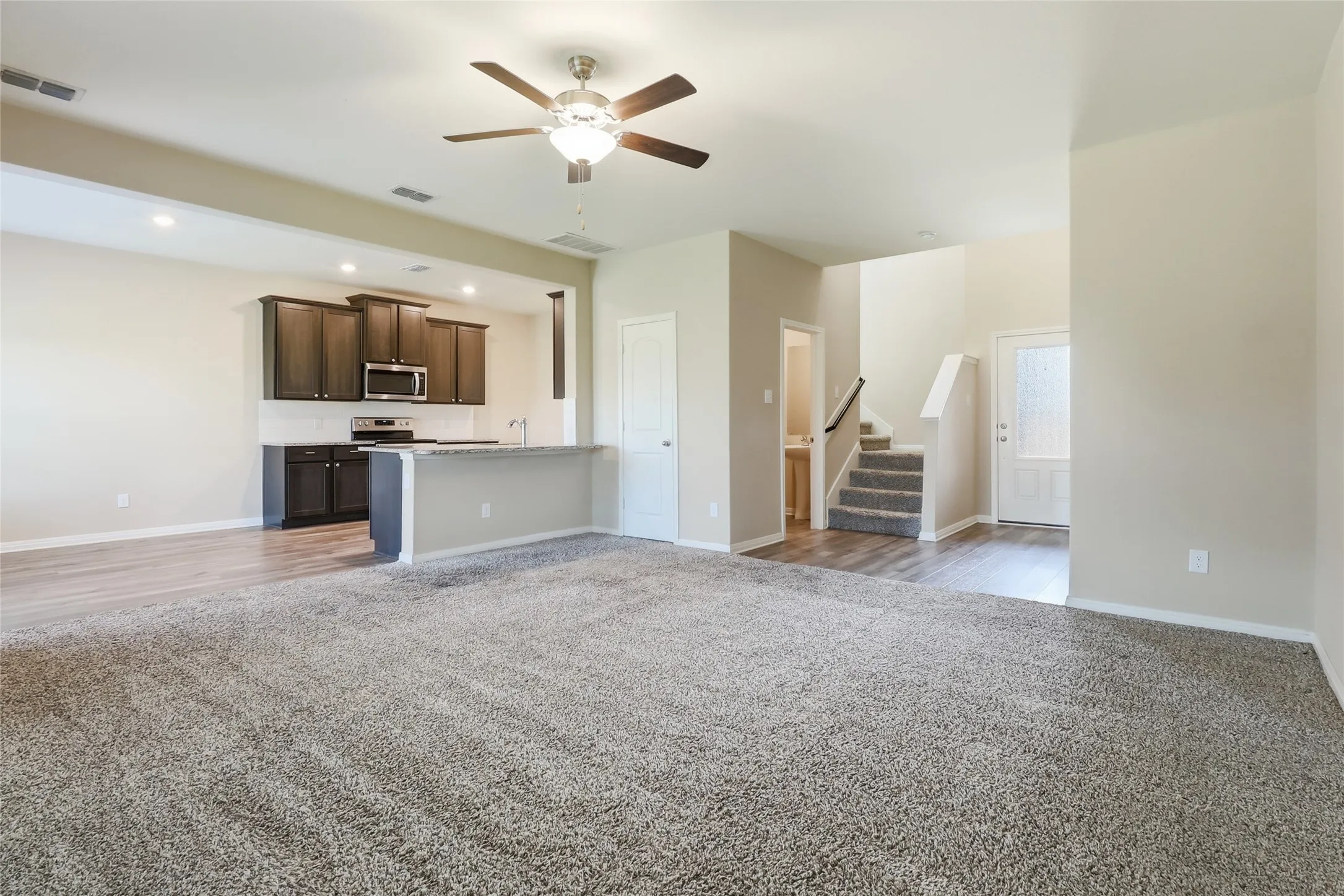 Open-concept living space featuring a kitchen with dark wood-finish cabinetry, built-in stainless steel appliances, and a breakfast bar