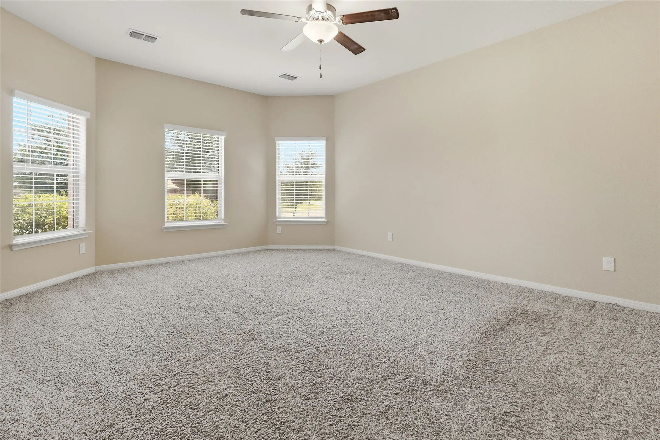 Spacious room featuring neutral wall paint, light-colored carpet, a ceiling fan with integrated lighting, and multiple windows with blinds