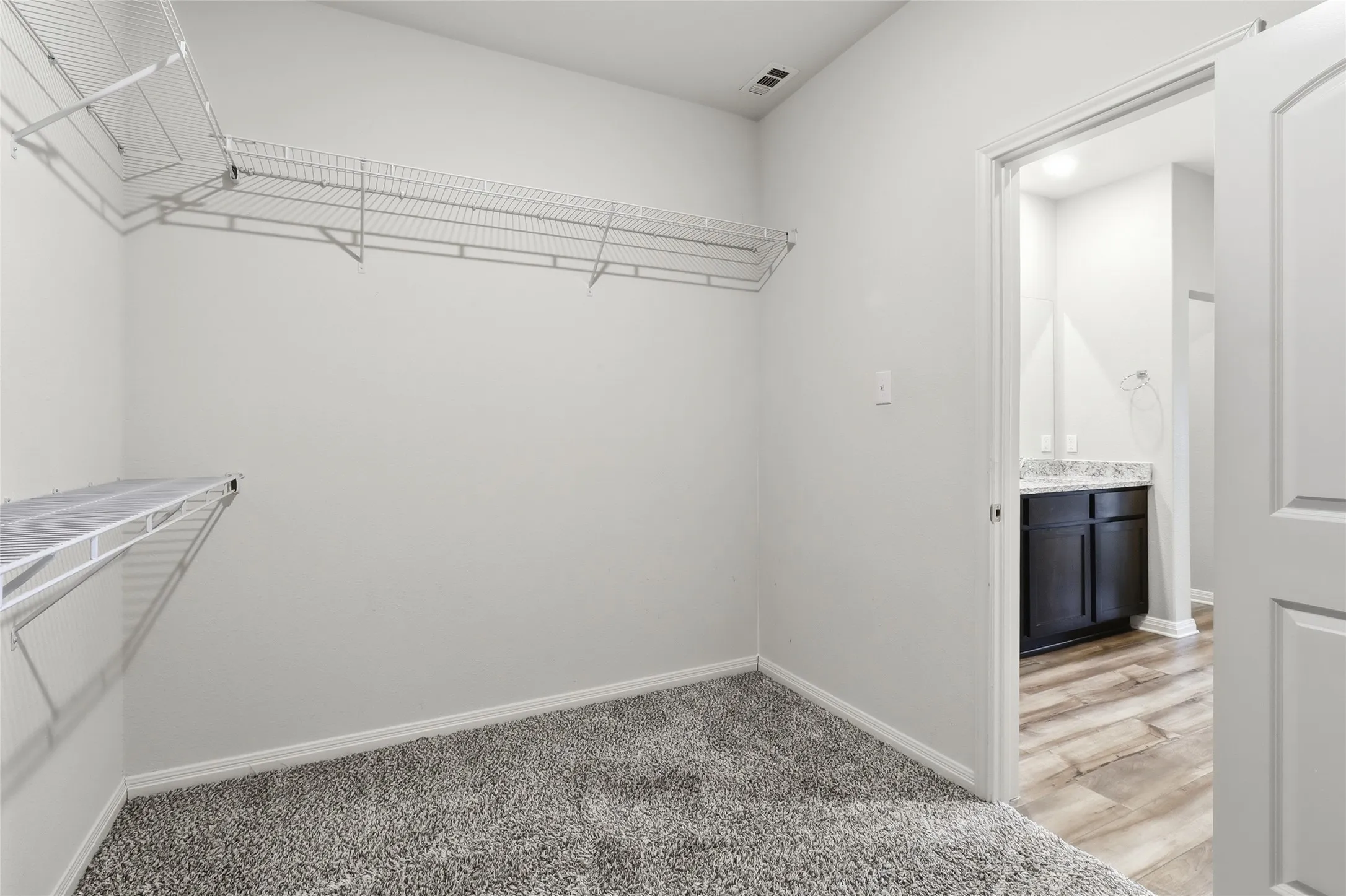 Walk-in closet featuring wire shelving, gray textured carpeting, and white baseboards