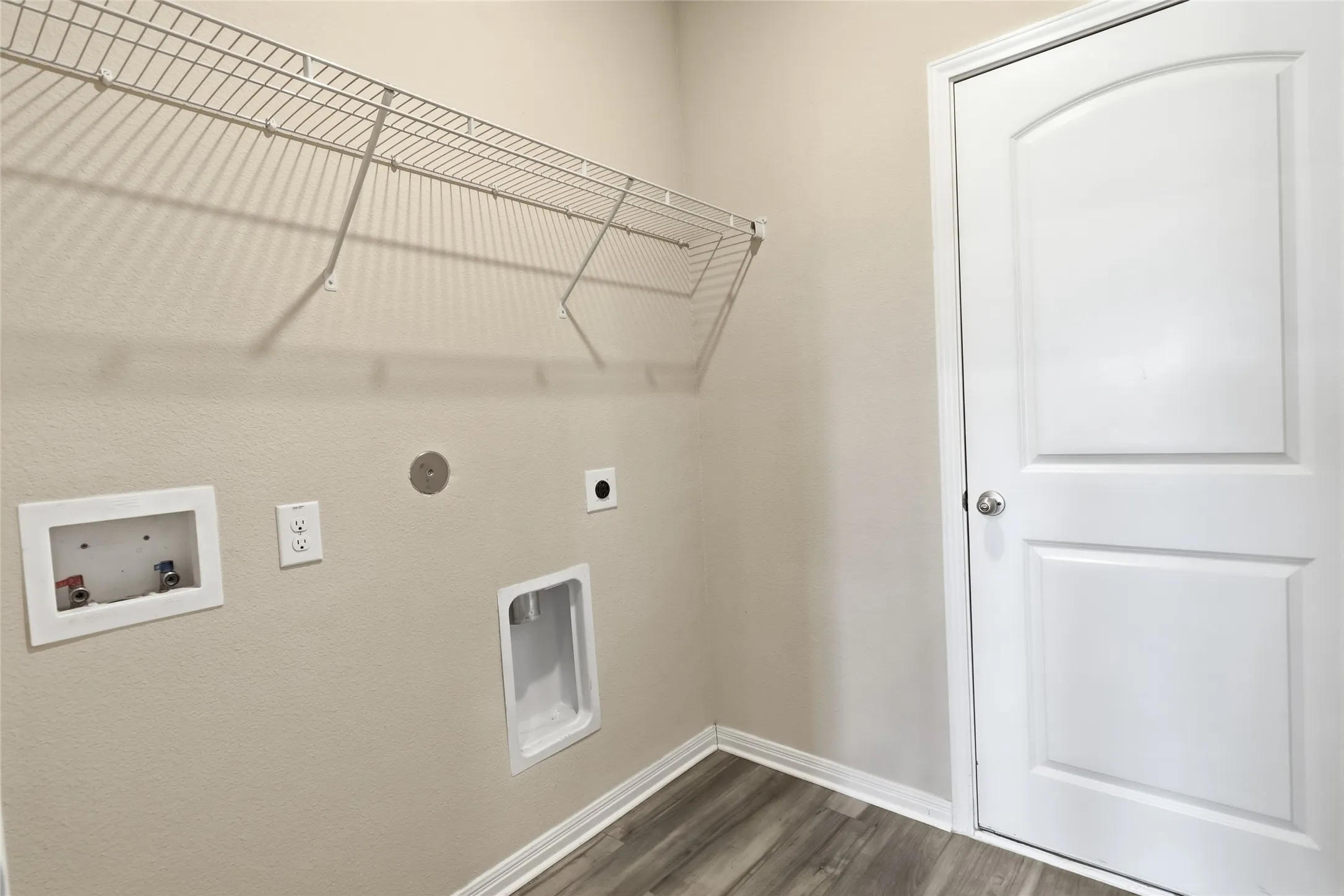 Dedicated utility space featuring wire shelving, wood-finish flooring, and a paneled interior door