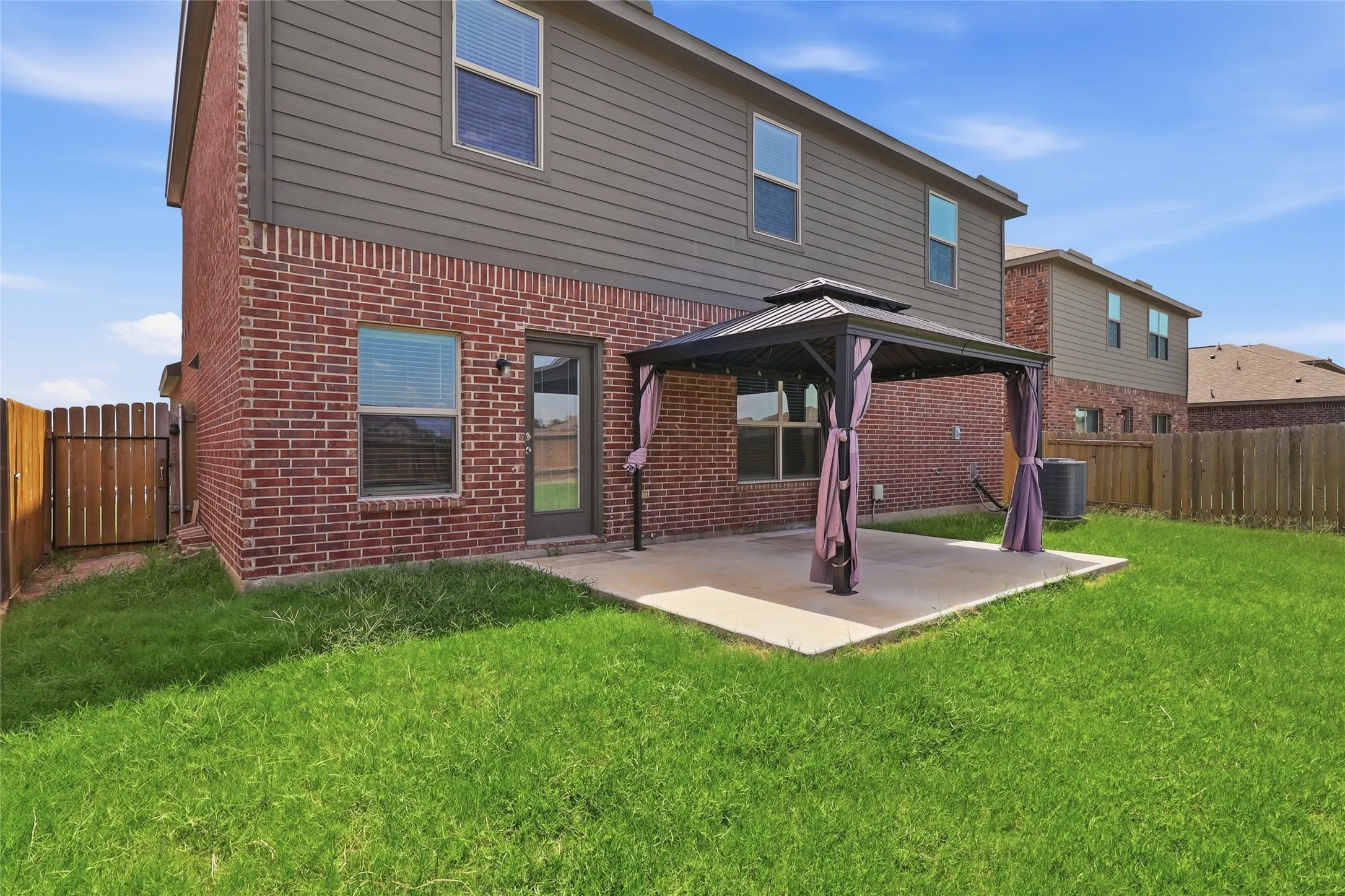 Rear exterior featuring brick and horizontal siding, a fenced yard, and a concrete patio with a permanent gazebo